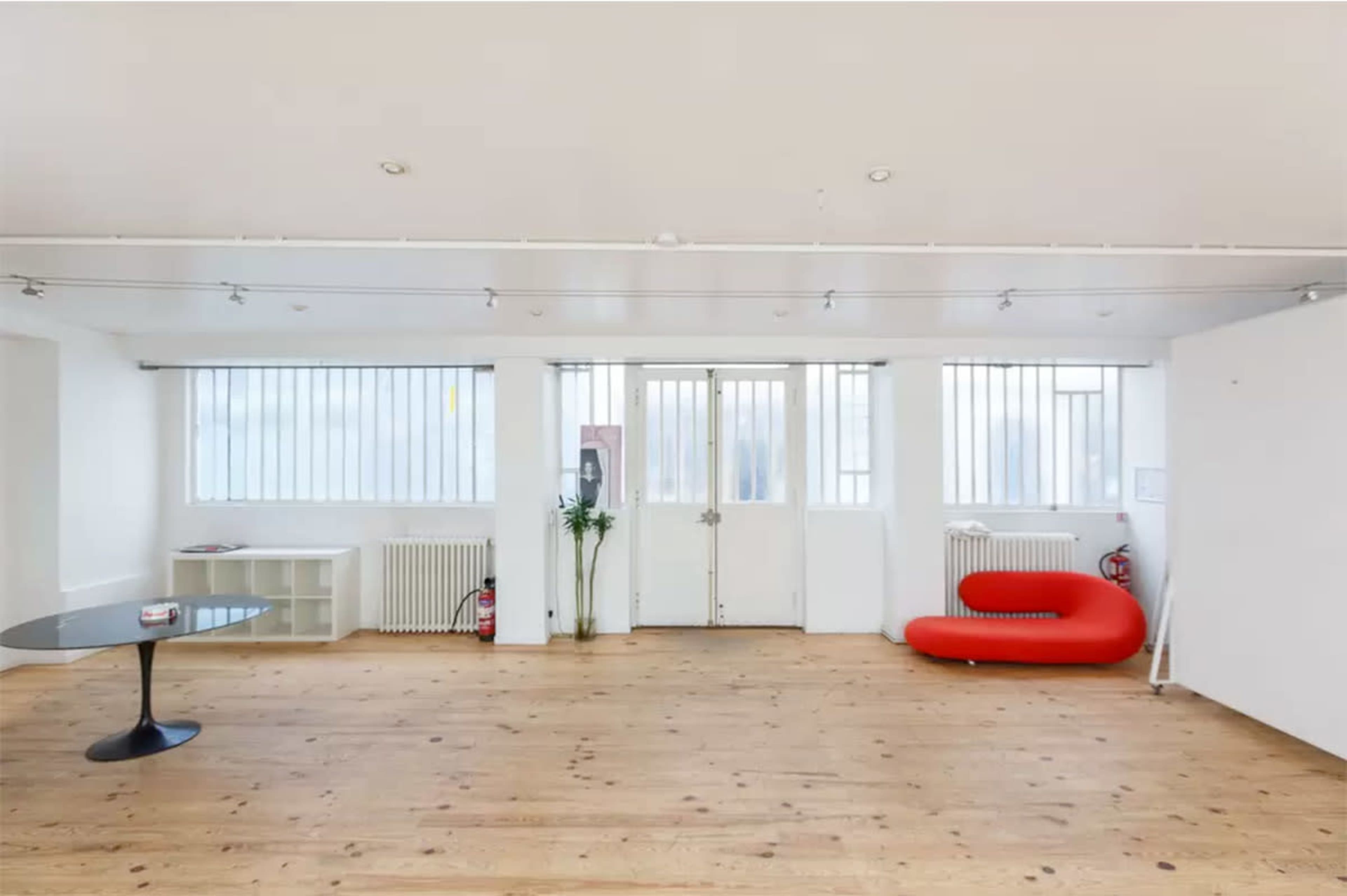 A minimalist interior space with wooden flooring, large windows, and a red modern sofa against the wall.