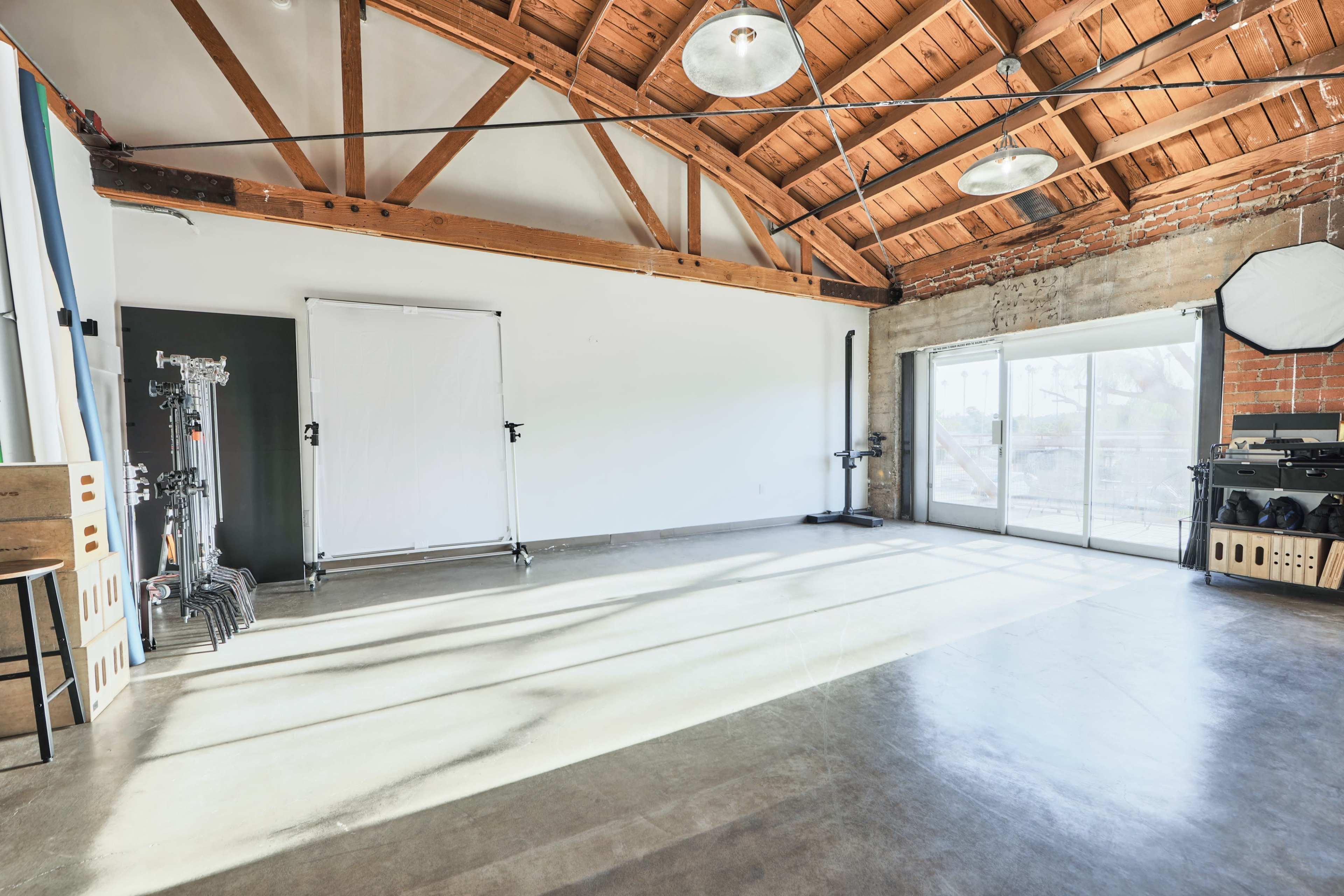 A spacious, industrial-style interior with exposed wooden beams, concrete flooring, and large windows letting in natural light.