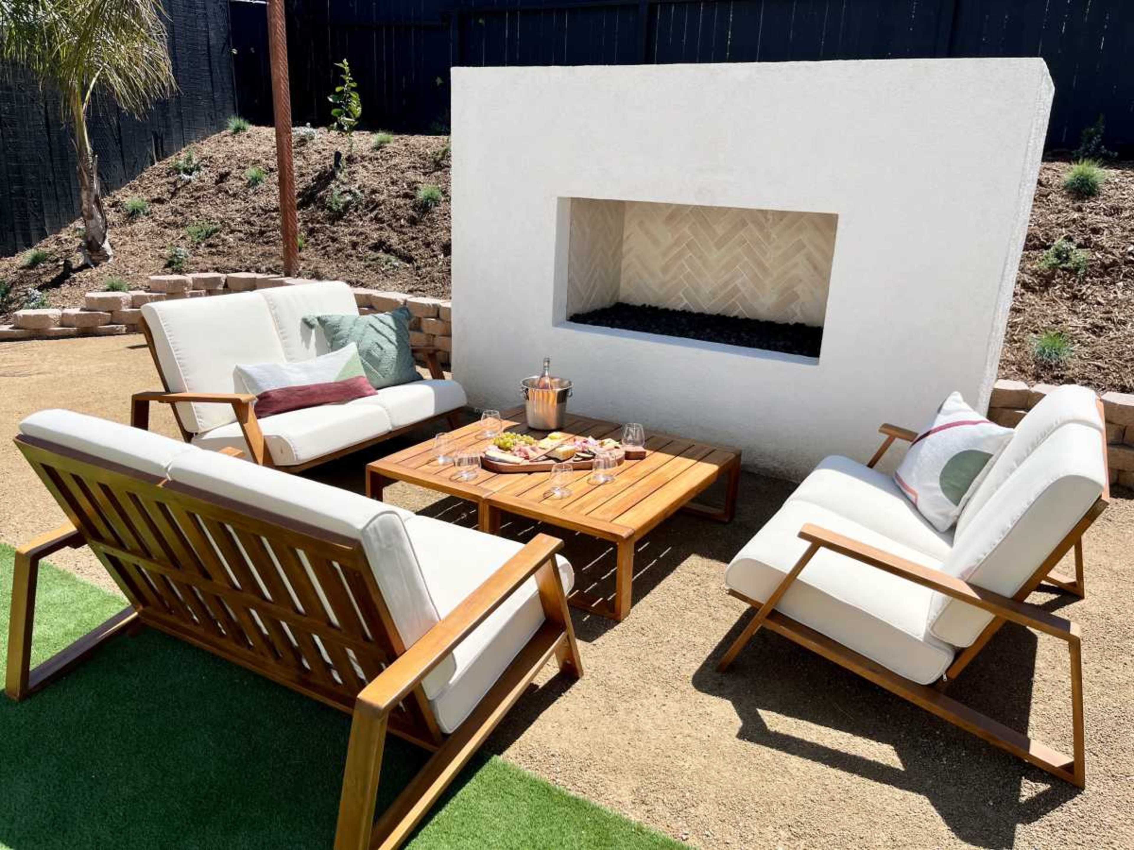 A patio seating area features four wooden chairs and a coffee table arranged around a modern white fireplace.