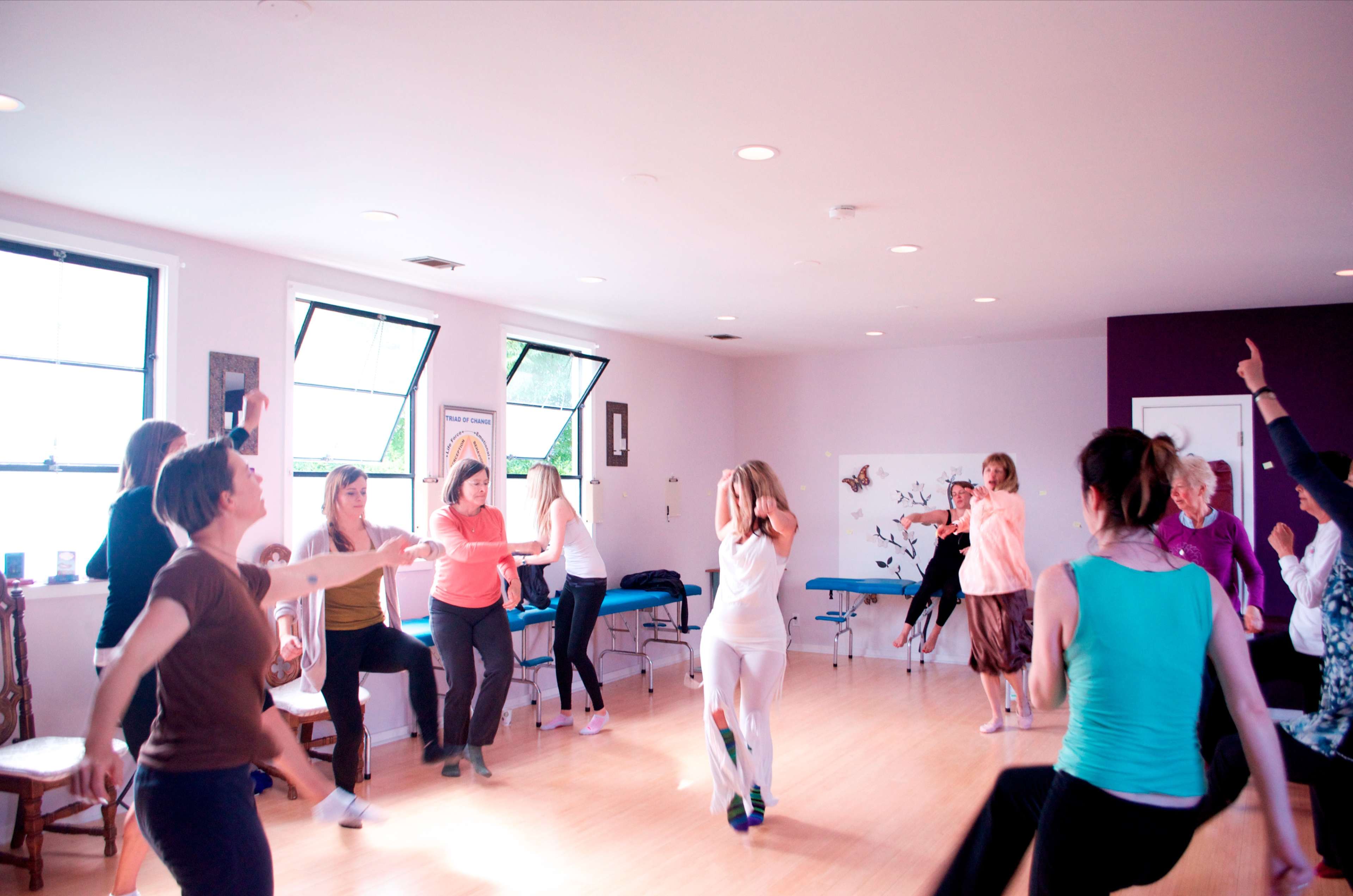 A group of people is engaged in a dance movement activity in a brightly lit studio.