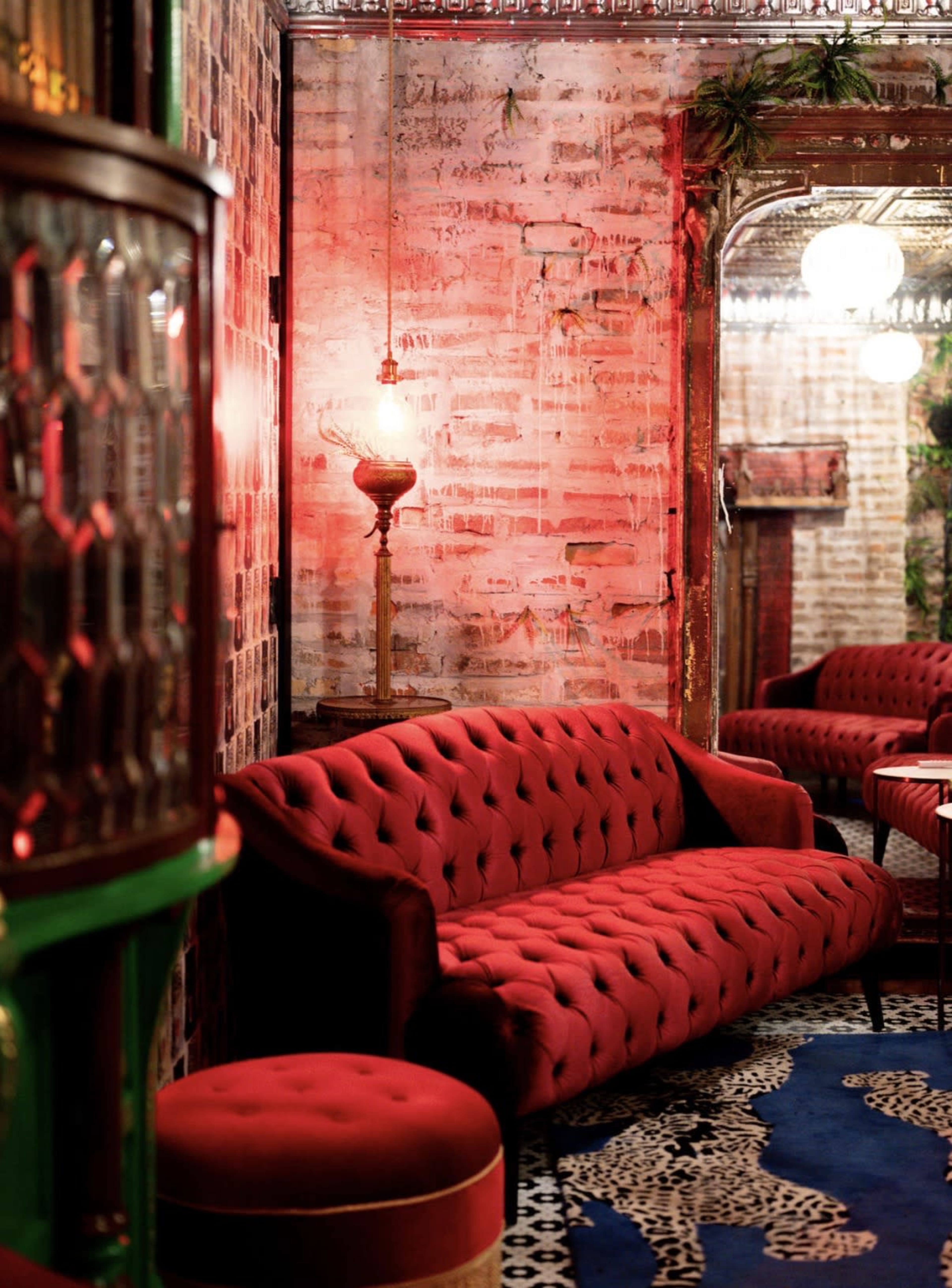 The image features a cozy lounge area with a red tufted sofa, a matching ottoman, and vintage decor elements illuminated by warm lighting.