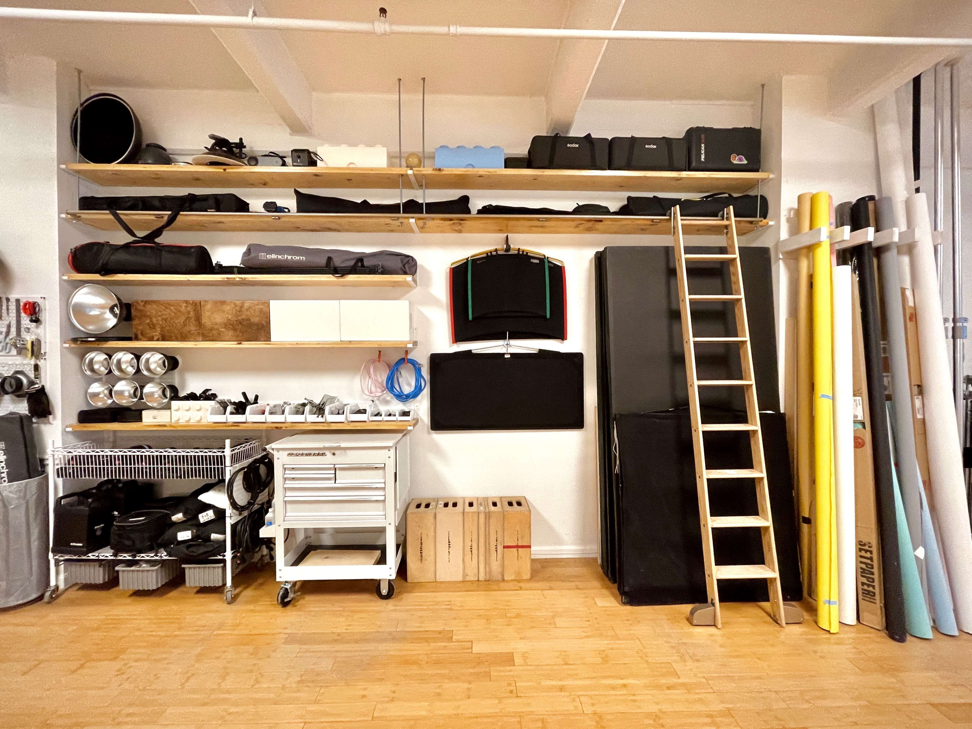 A neatly organized storage space with shelves holding various equipment, a ladder leaning against the wall, and a cart with tools.