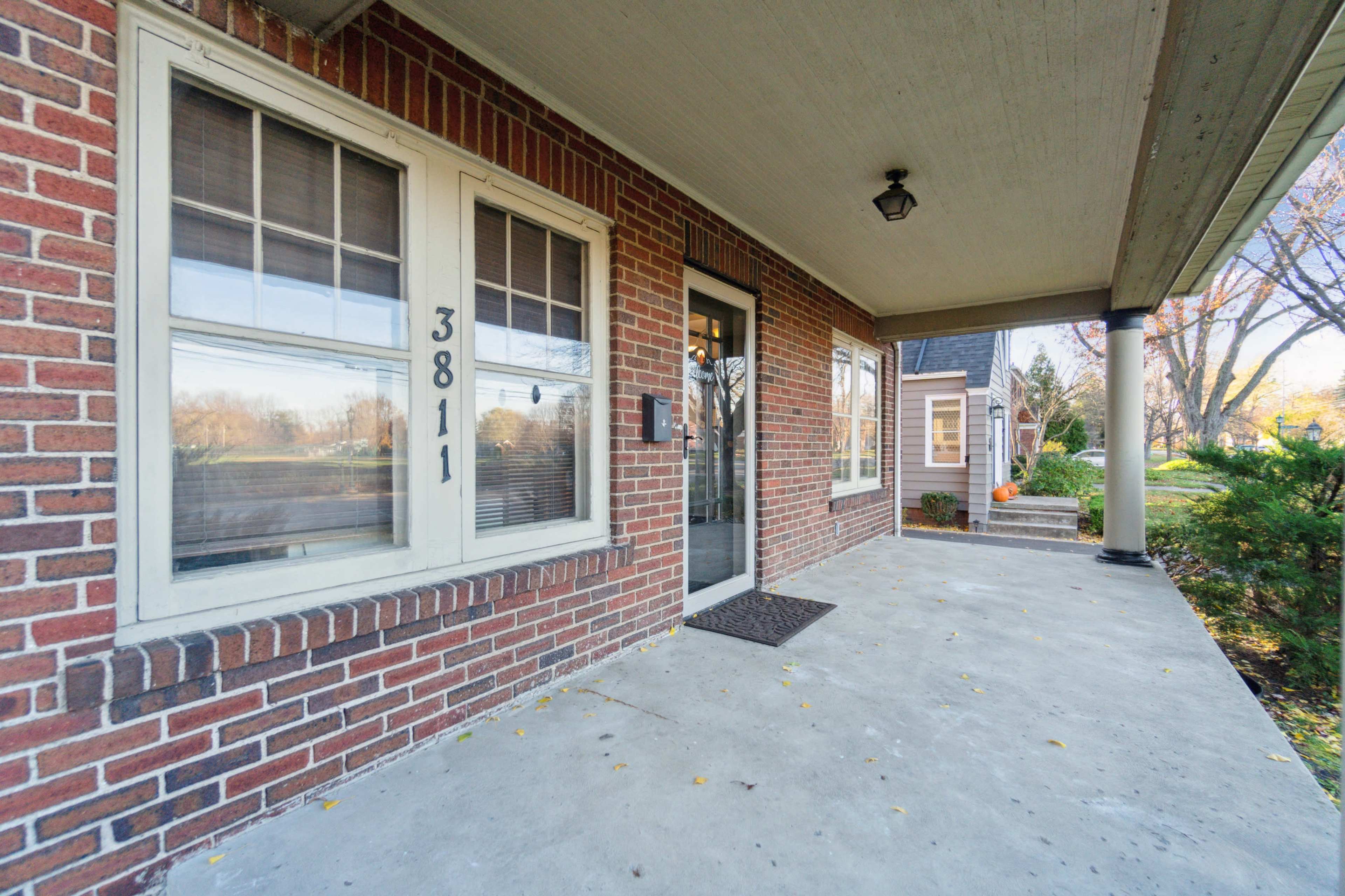 The image shows a brick porch entrance with a glass door and large windows, featuring a house number displayed prominently.