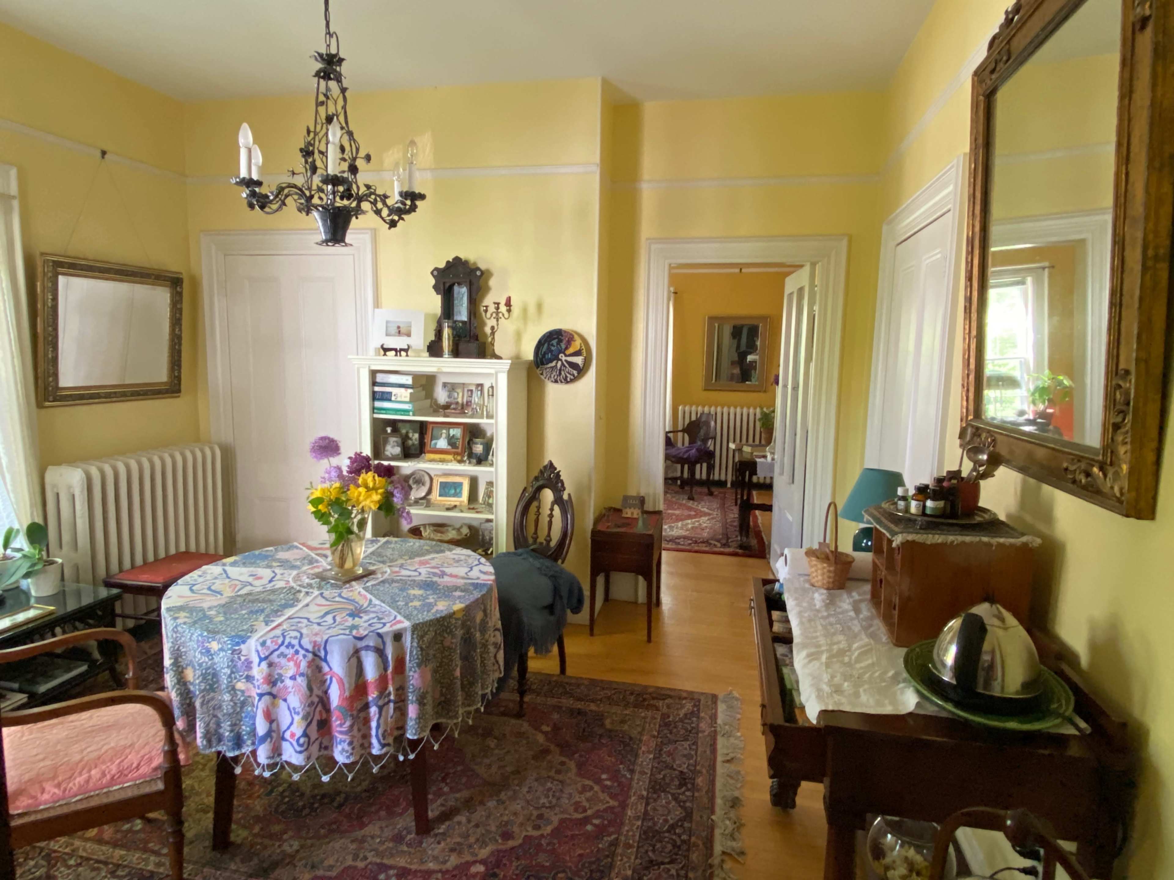 A yellow-painted dining room with a table covered by a patterned cloth, surrounded by wooden chairs, and framed by multiple doorways leading to adjacent rooms.