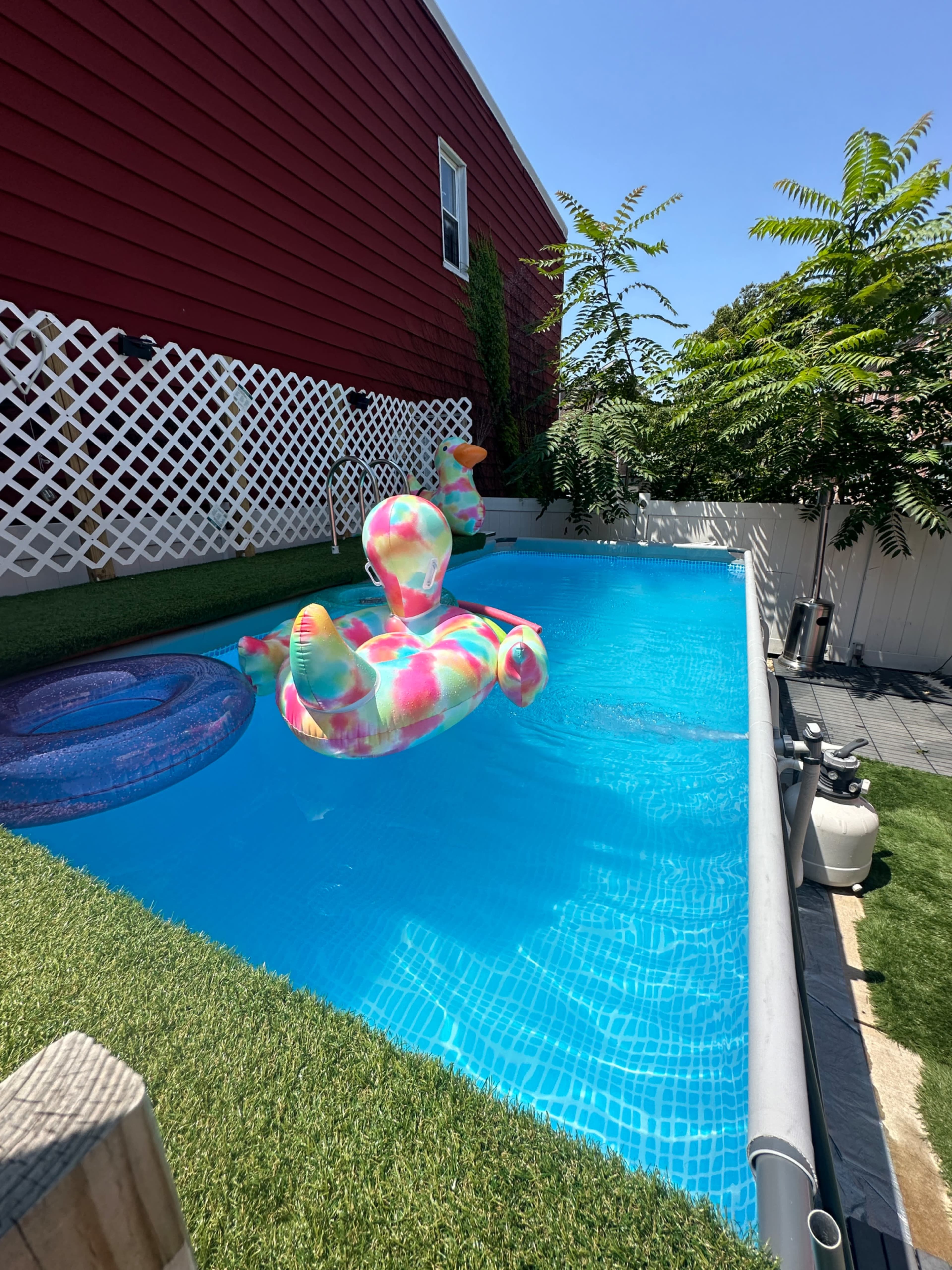 A colorful inflatable float sits in a rectangular swimming pool surrounded by green grass and a wooden fence.