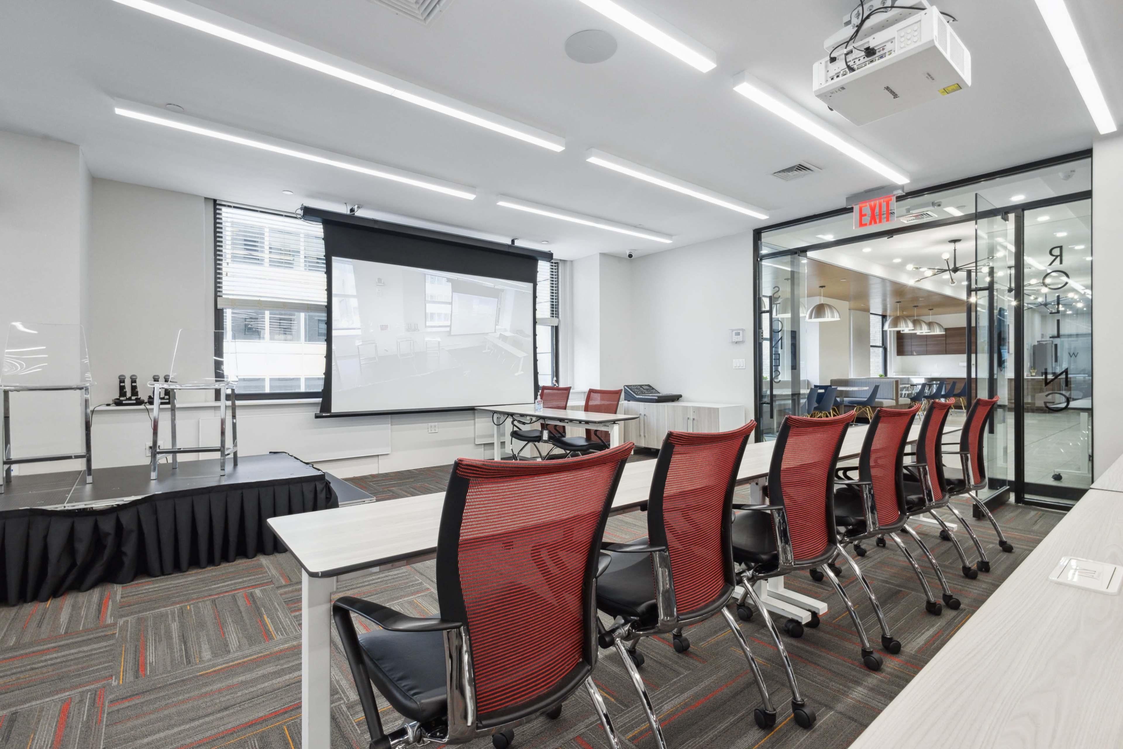 The image shows a modern conference room equipped with a projector, a screen, and several red mesh chairs arranged in rows.