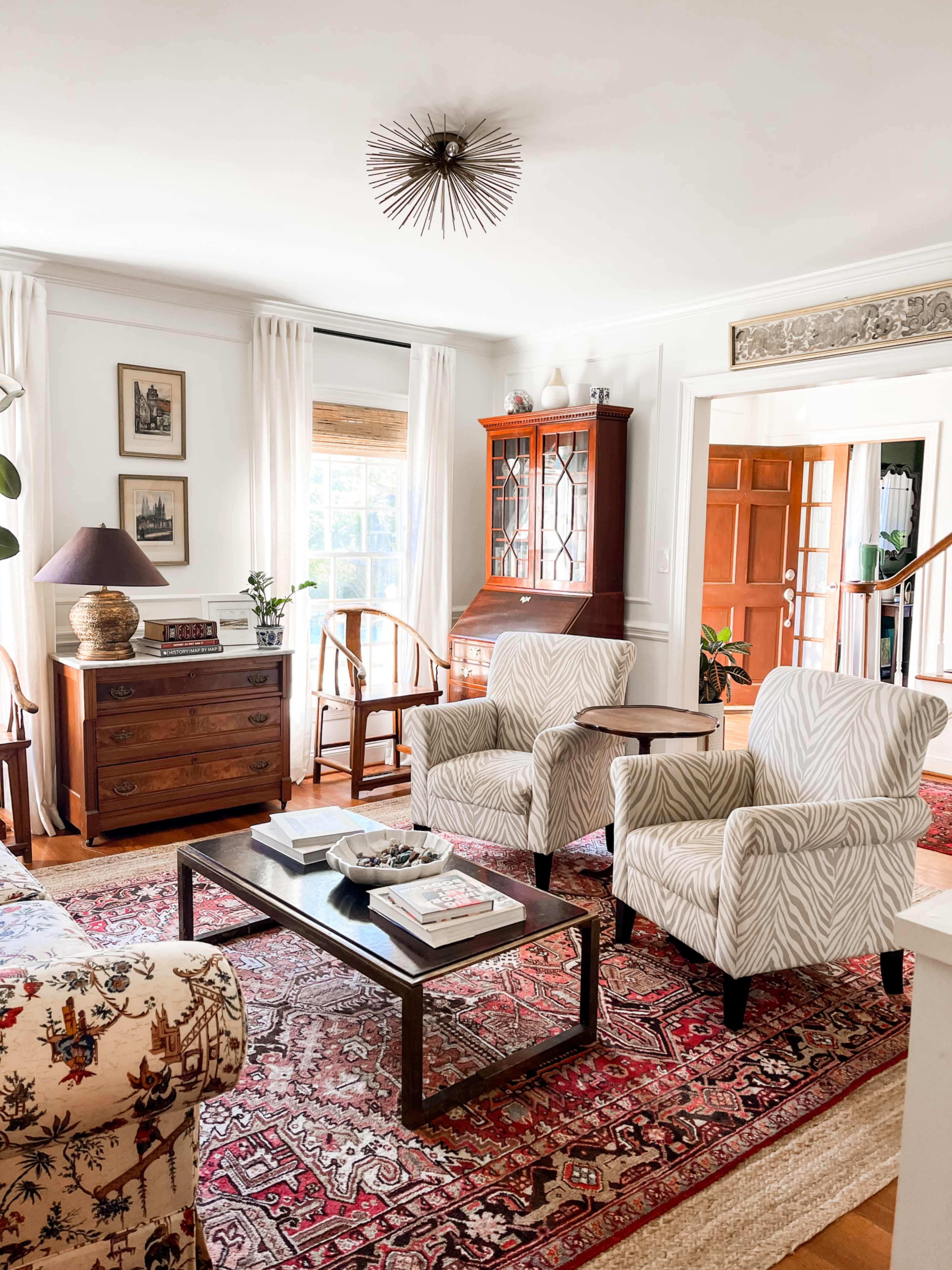 The living room features a patterned rug, two upholstered chairs, a wooden coffee table, and a cabinet against a bright window.