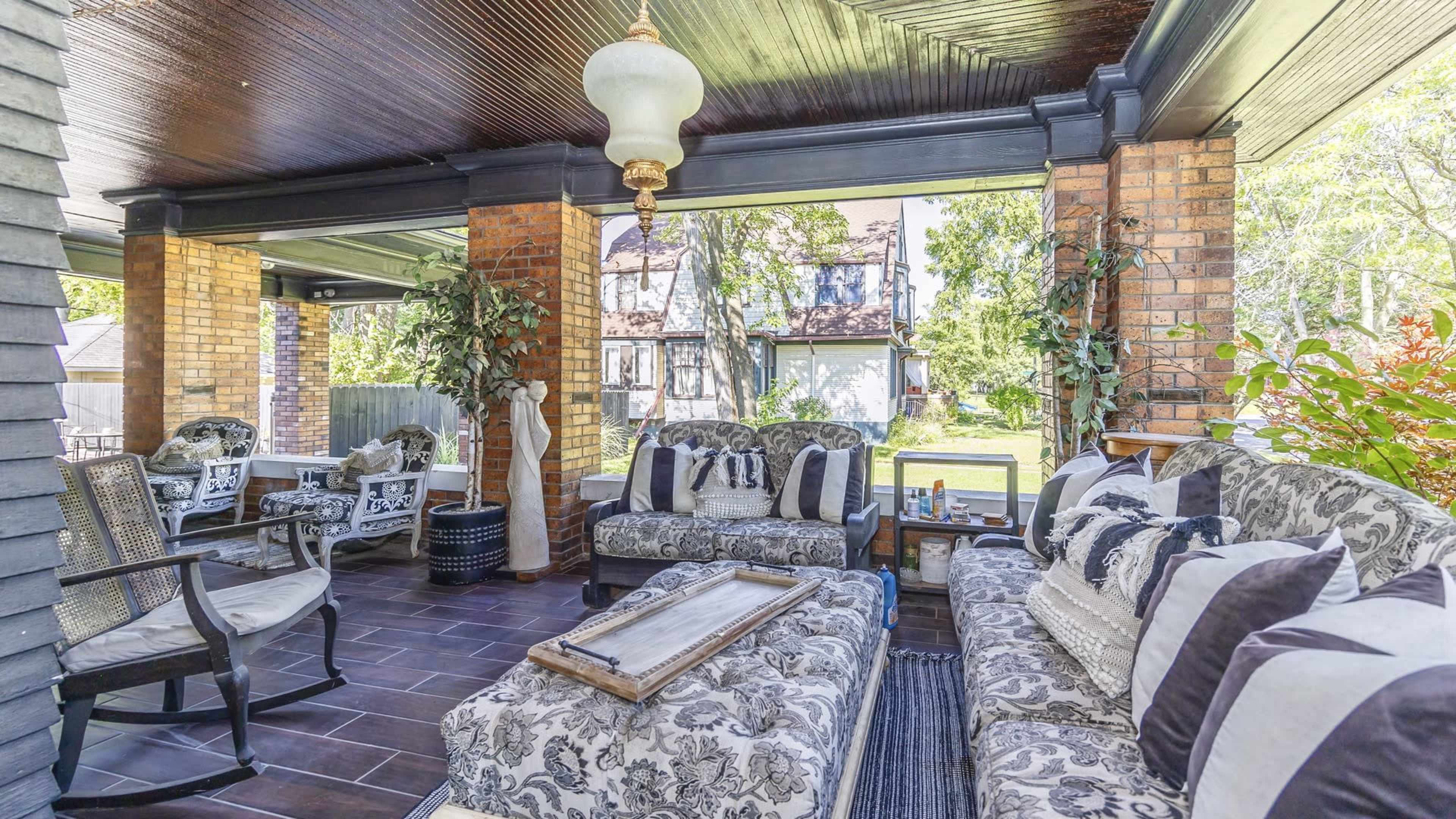 A covered outdoor living area with floral-patterned furniture, a coffee table, and large windows overlooking a garden.