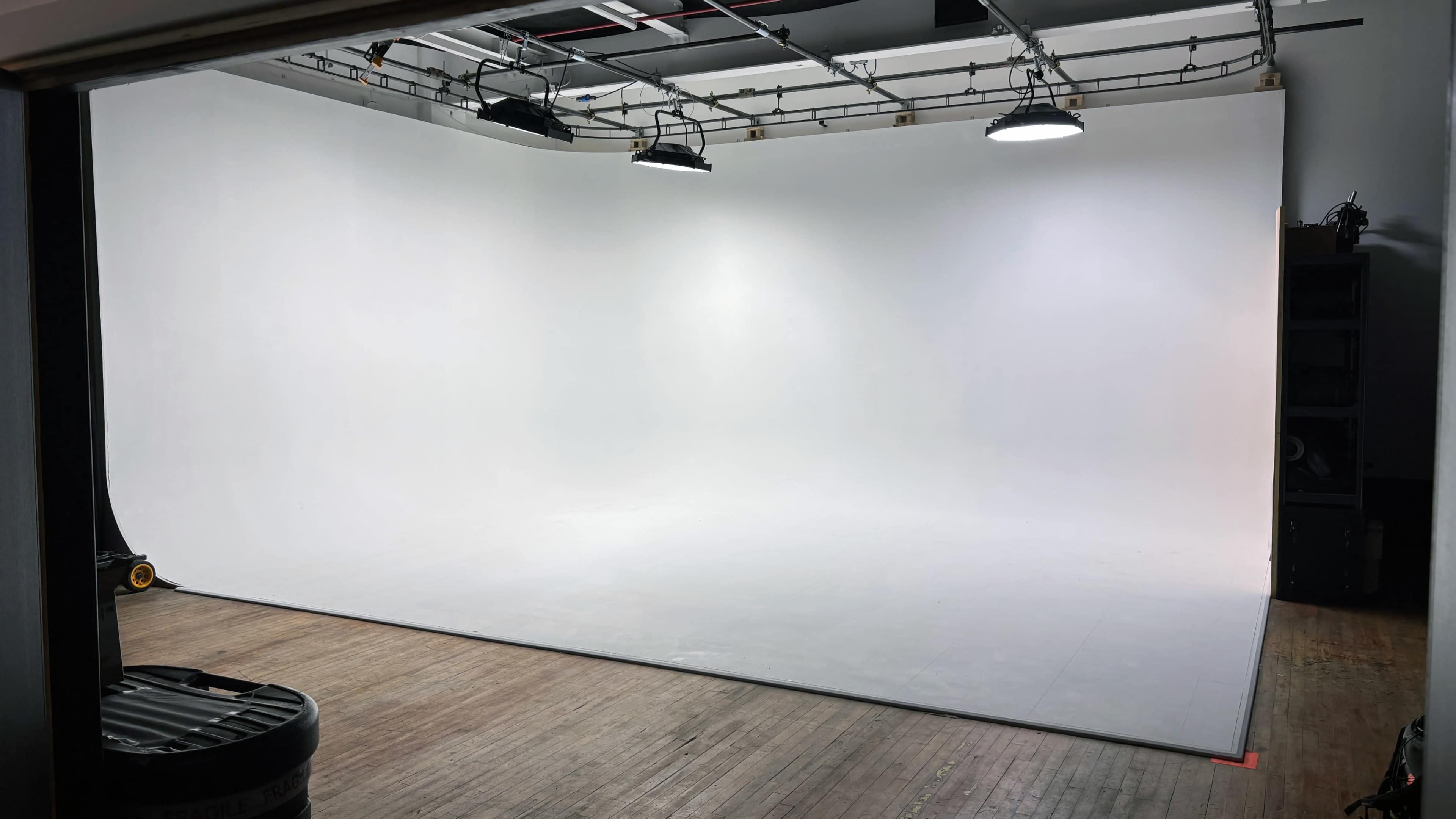 The image shows a spacious photography studio with a seamless white backdrop and overhead lighting.