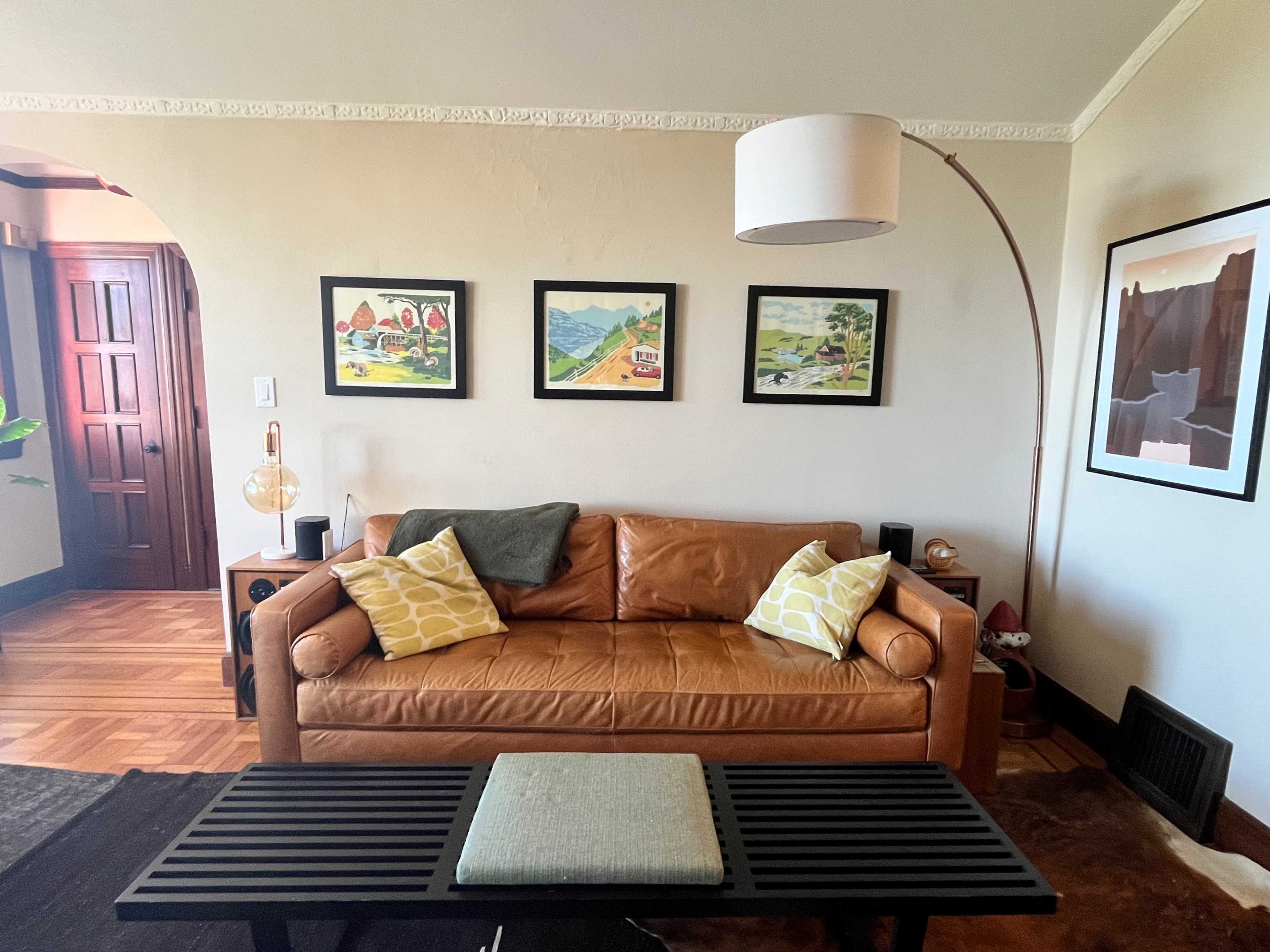 A living room with a brown leather sofa adorned with yellow-patterned pillows, a black coffee table, and framed artwork on the walls.