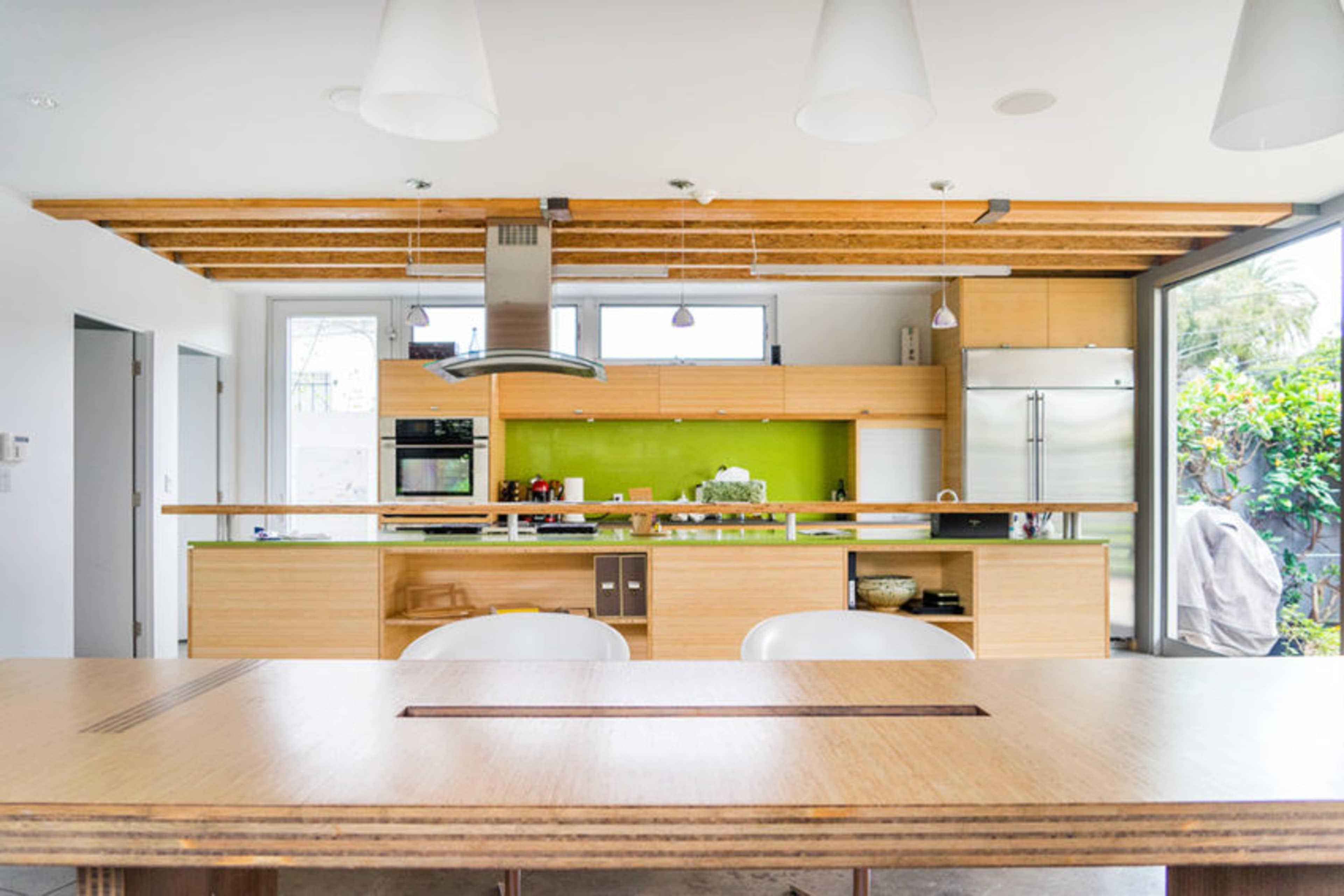 The image shows a modern kitchen with a wooden beam ceiling, green accent wall, and stainless steel appliances.