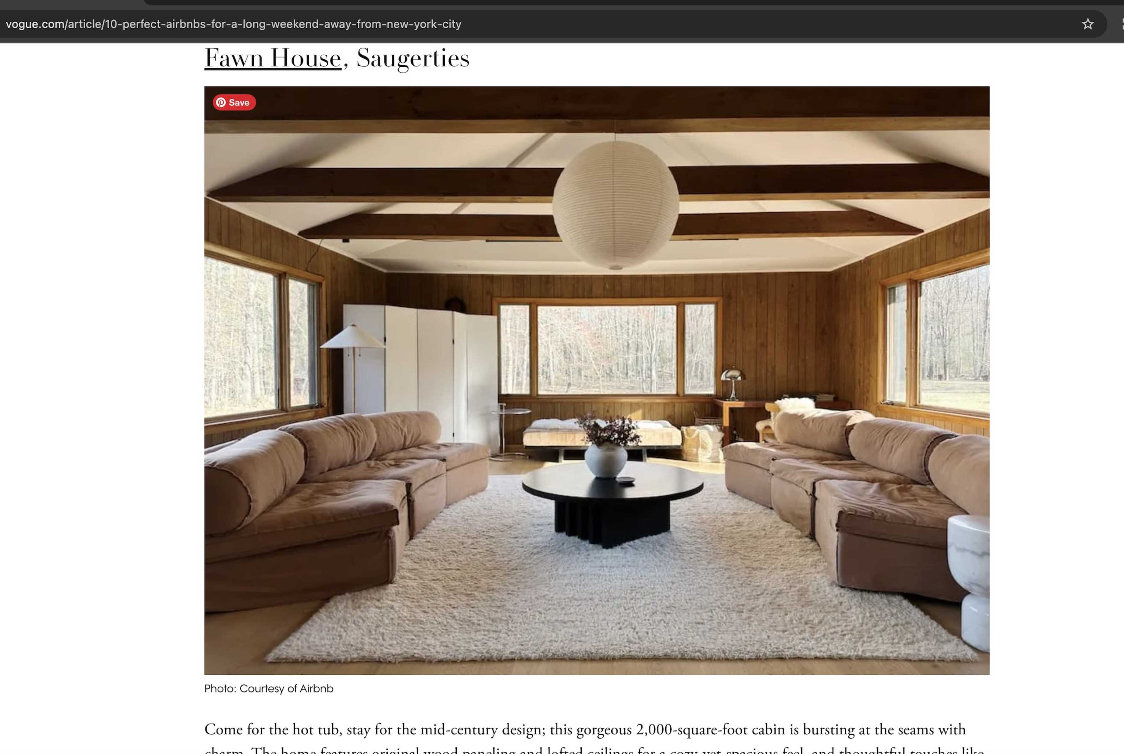 The image shows a spacious cabin interior featuring mid-century modern furnishings, large windows, and a central seating area with a round coffee table.