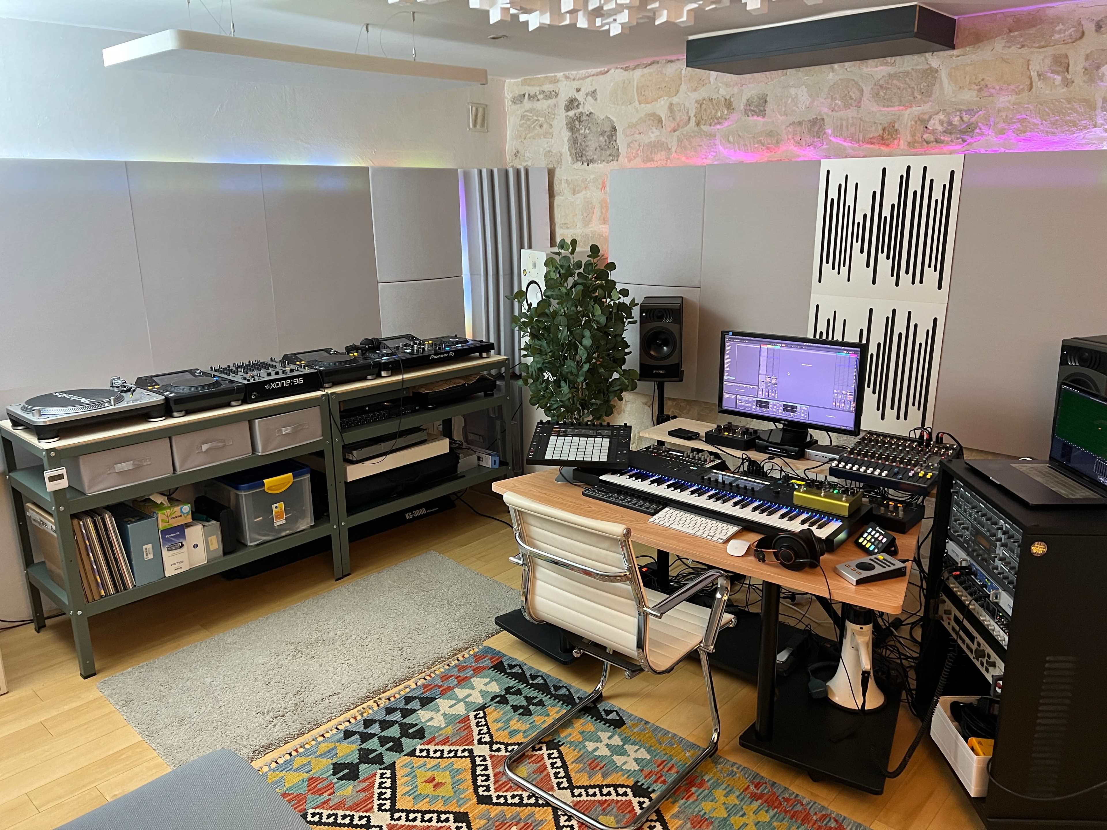 A music production studio featuring turntables, a keyboard, various audio equipment, and a desk with a computer setup.