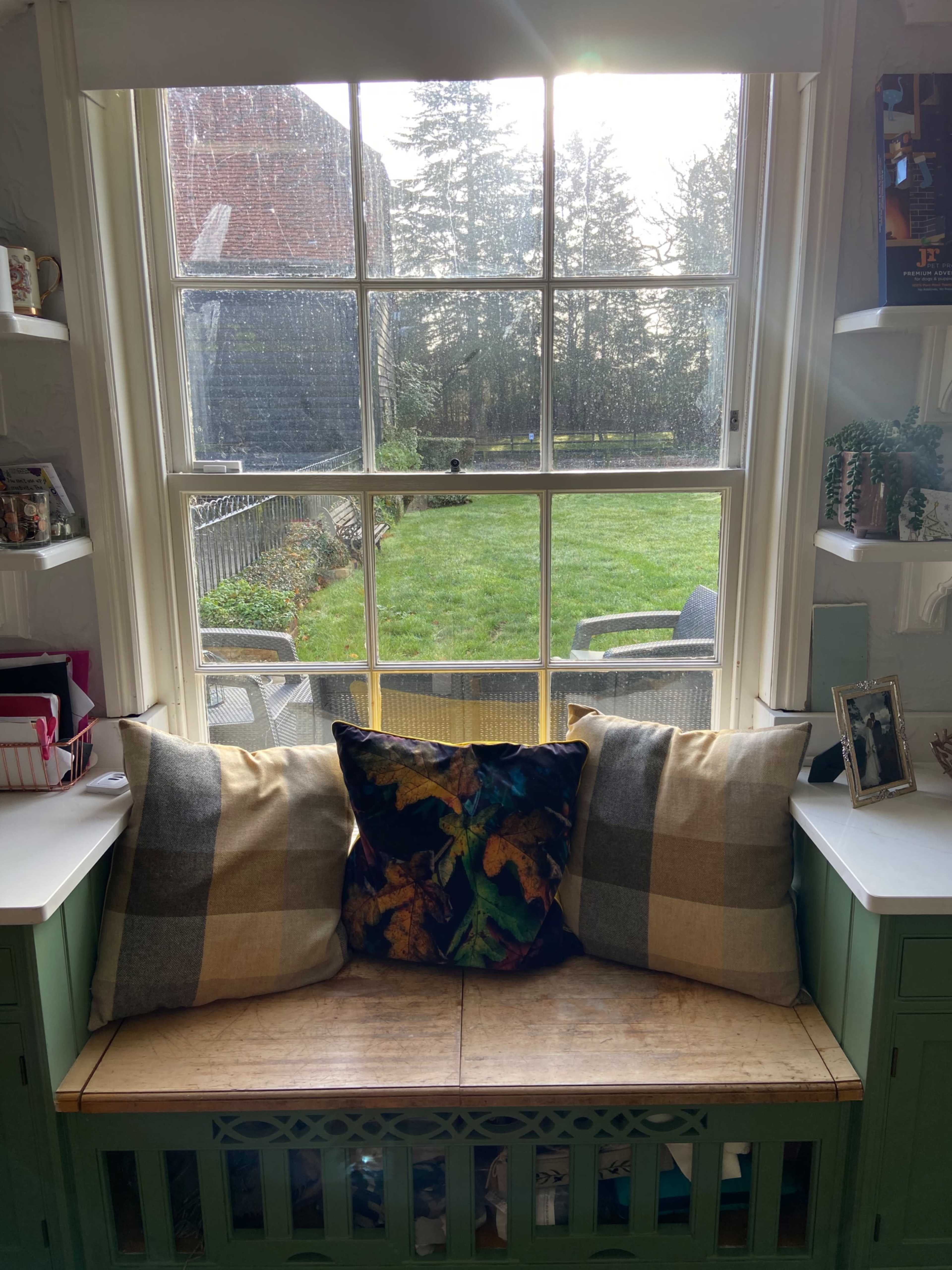 A cozy window nook features two patterned pillows and looks out onto a green lawn surrounded by trees.