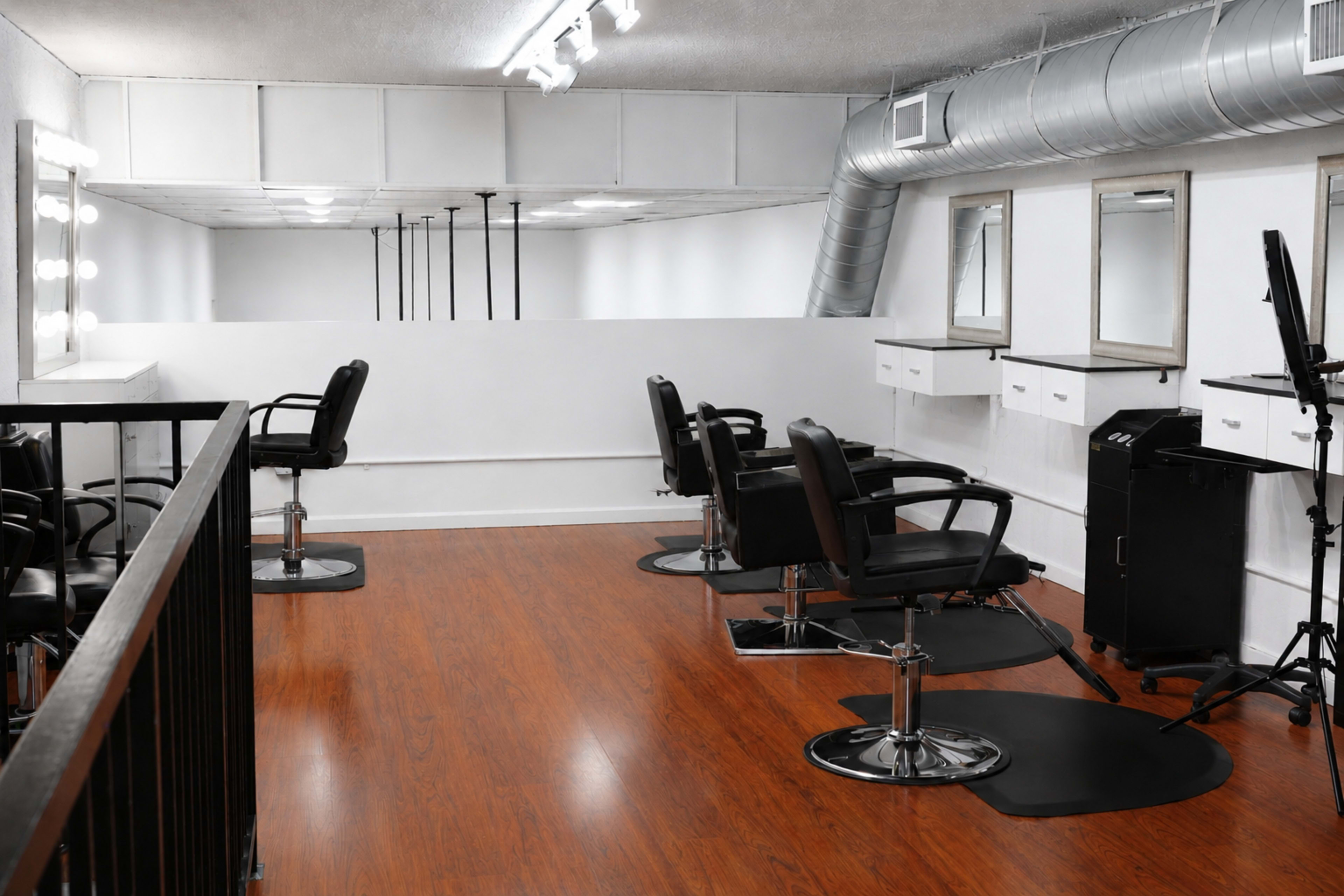 The image shows a modern hair salon featuring several black styling chairs, mirrors, and a sleek wooden floor.