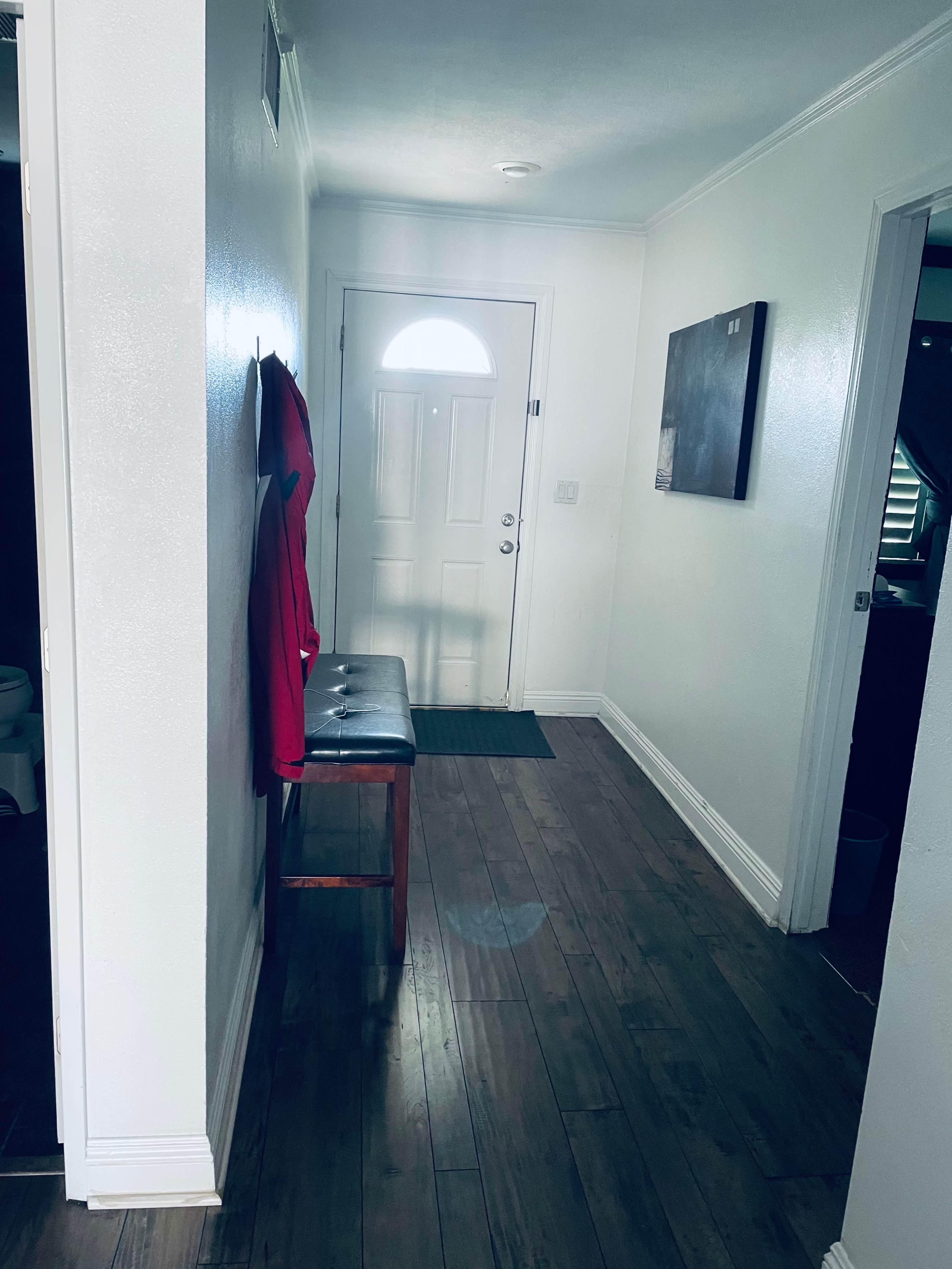 A narrow hallway with a bench, a red coat hanging on the wall, and a front door at the end.