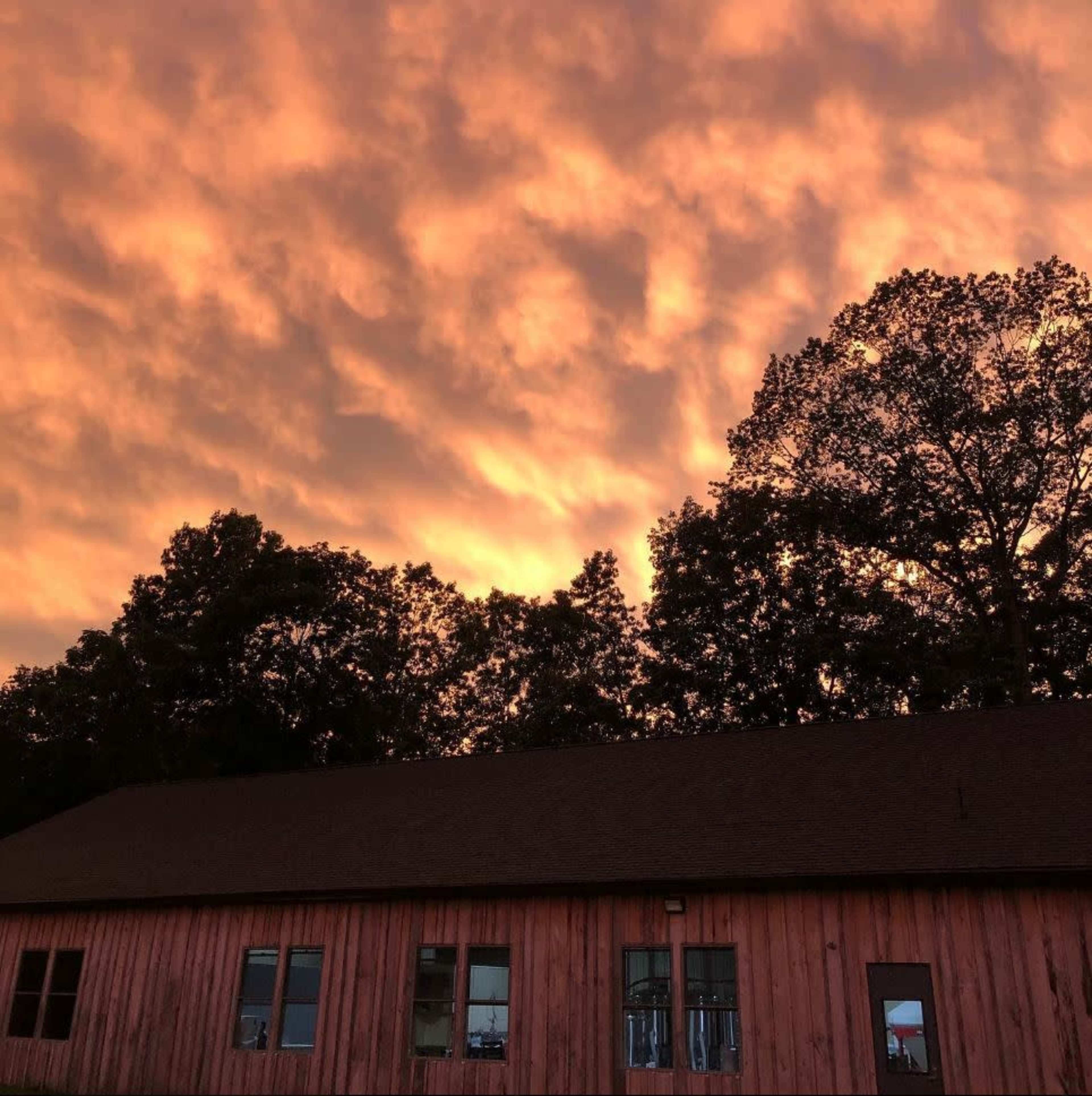 A wooden building is silhouetted against a vibrant orange and pink sky at sunset, with trees in the background.