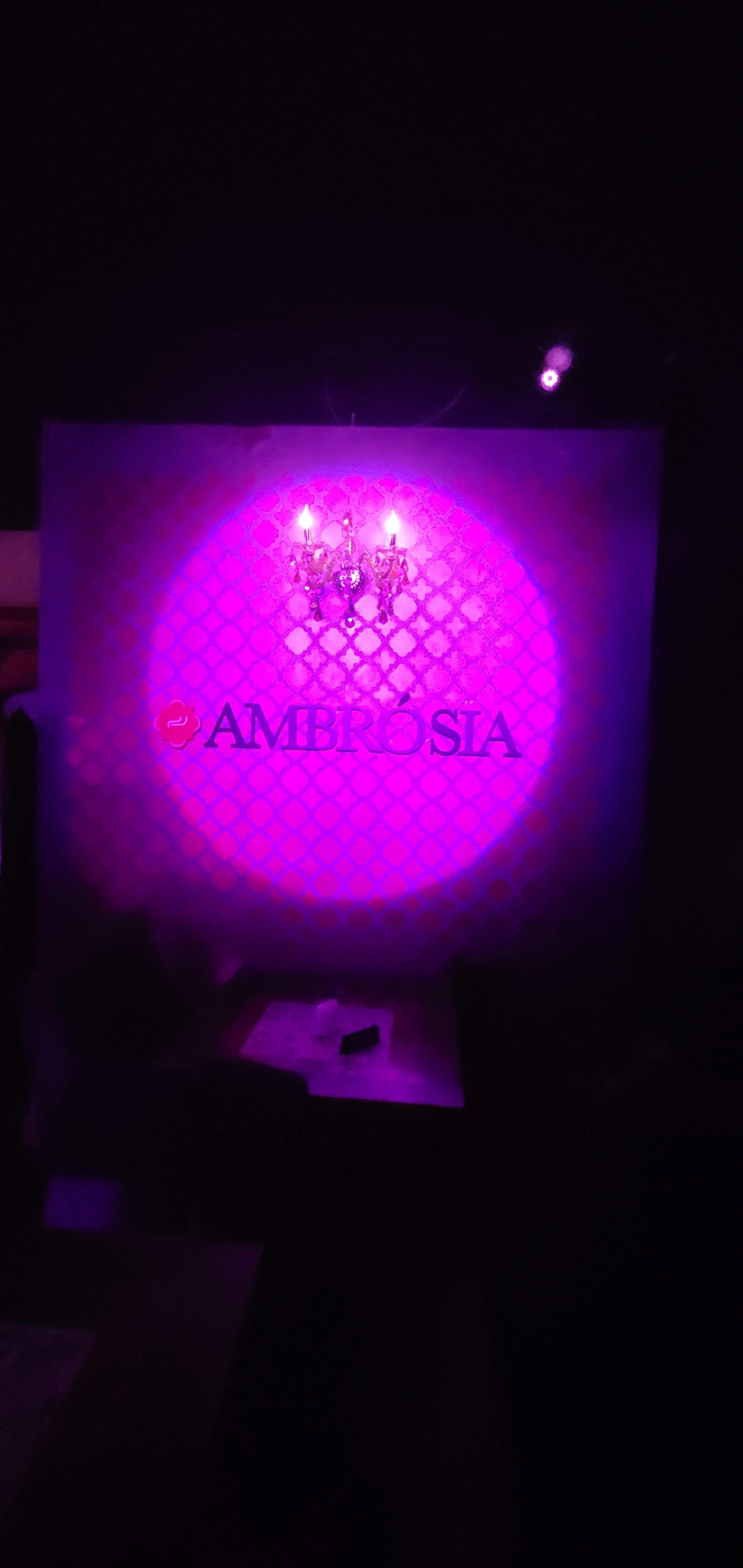 The image shows a dimly lit venue with a purple spotlight illuminating the "AMBRIOSIA" logo on a wall.