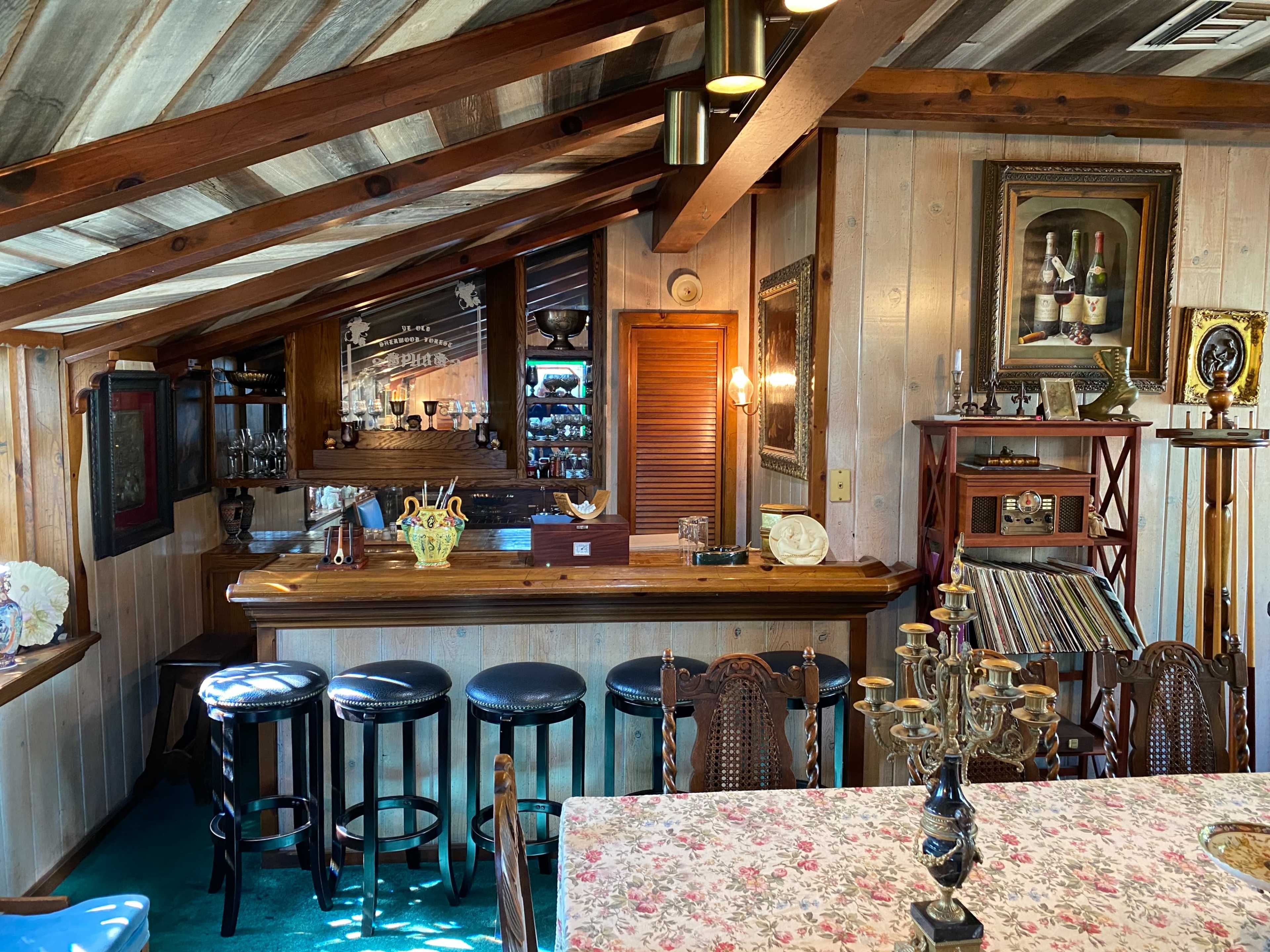 A rustic interior of a cafe with a wooden bar area, several stools, and a dining table adorned with a floral tablecloth.