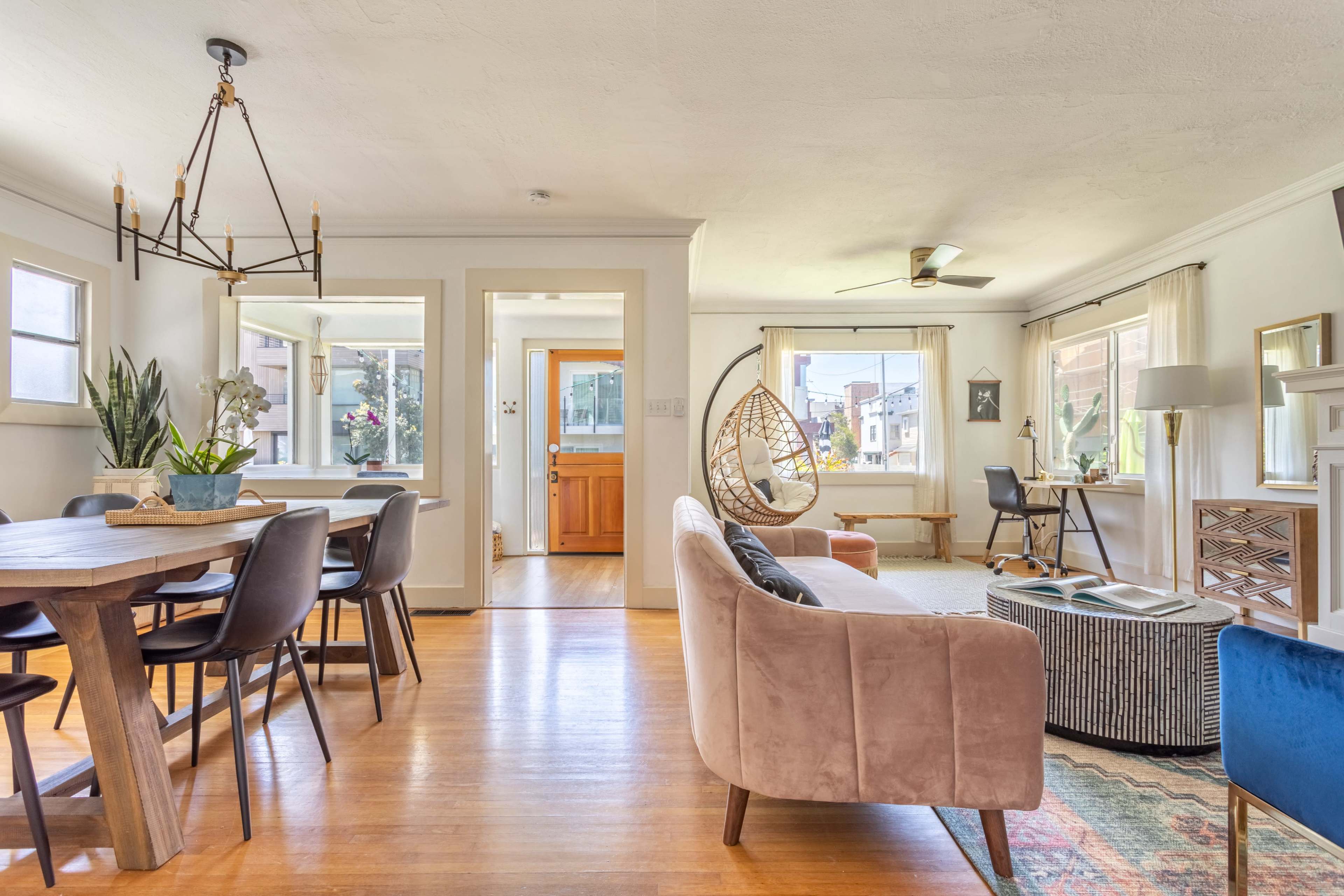 A bright and inviting open-concept living space featuring a dining area with a wooden table, a cozy seating arrangement, and a workspace by a window.