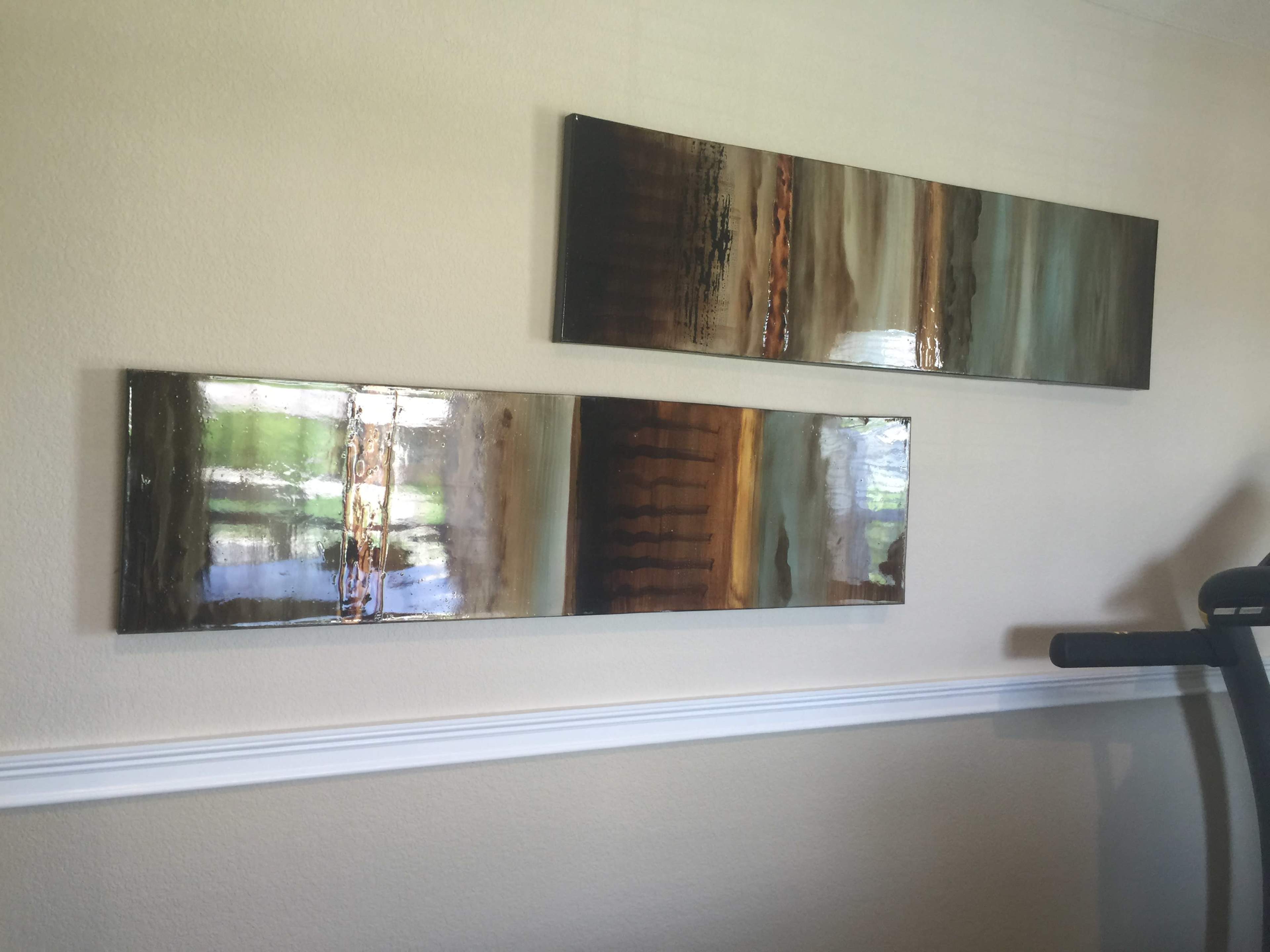 Two rectangular artworks are mounted on a beige wall, featuring abstract designs in earthy tones.