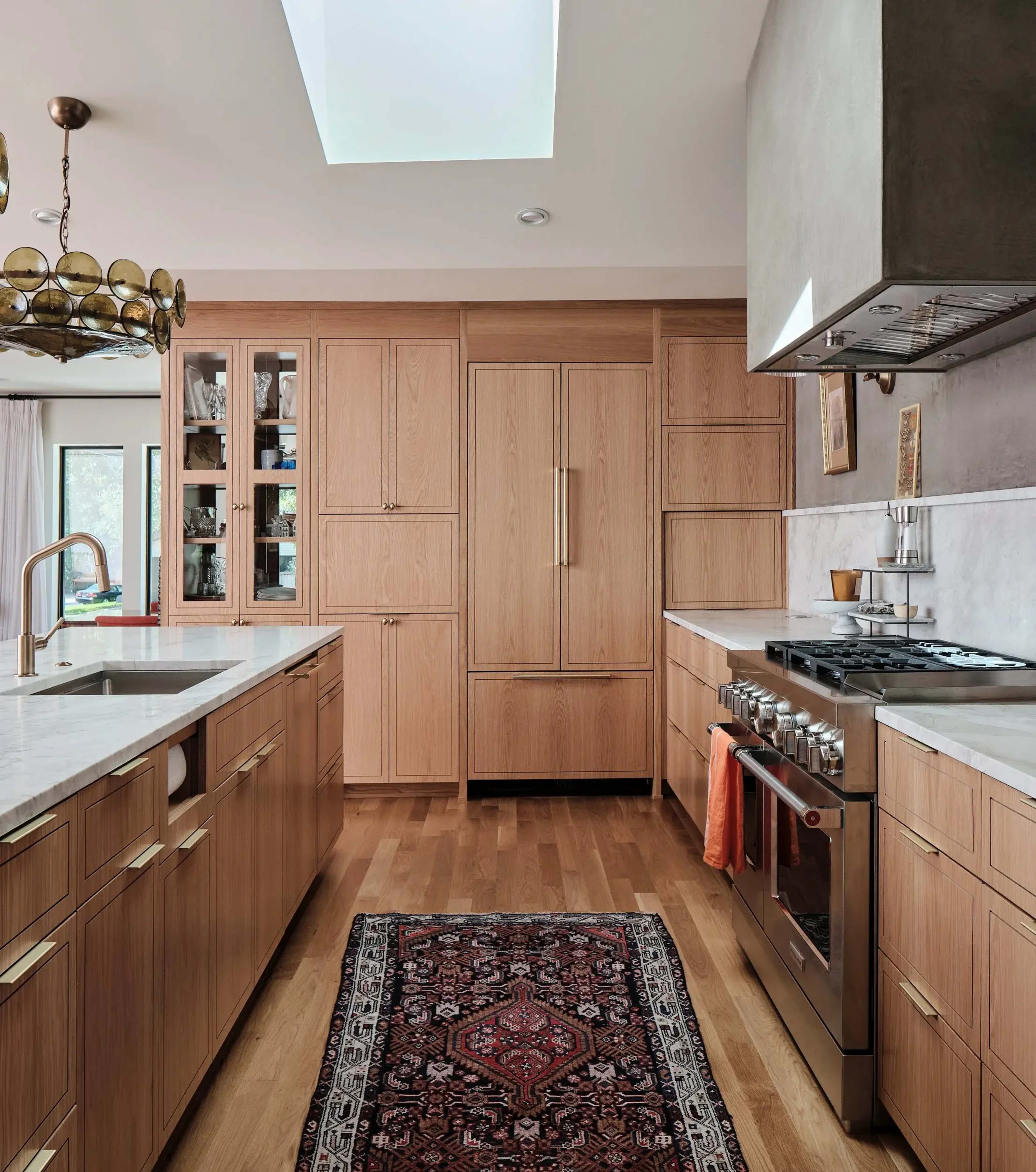 The kitchen features wooden cabinetry, marble countertops, a stainless steel stove, and a patterned rug on a hardwood floor.