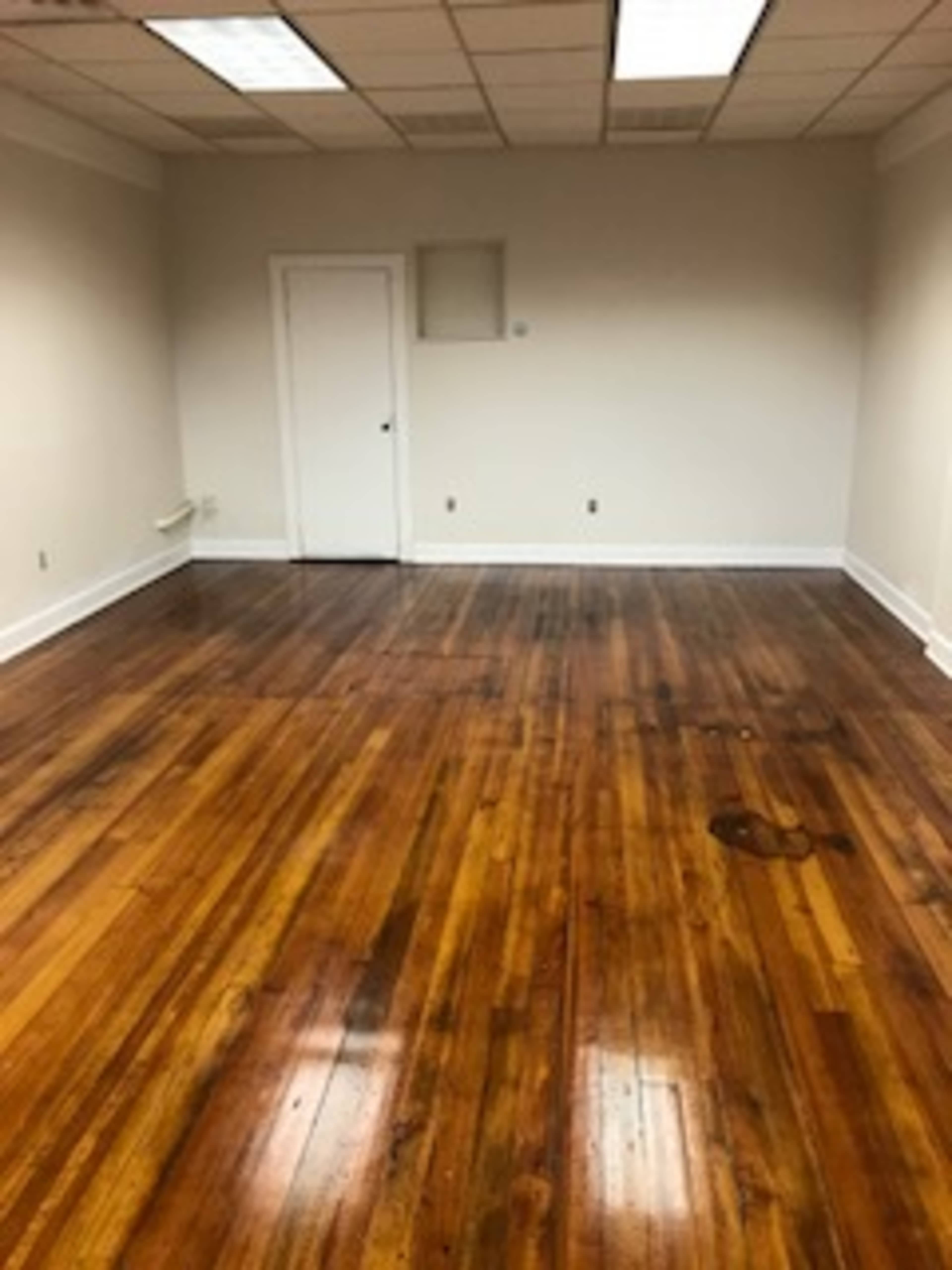 The image shows an empty room with polished wooden floors and a door on one wall.