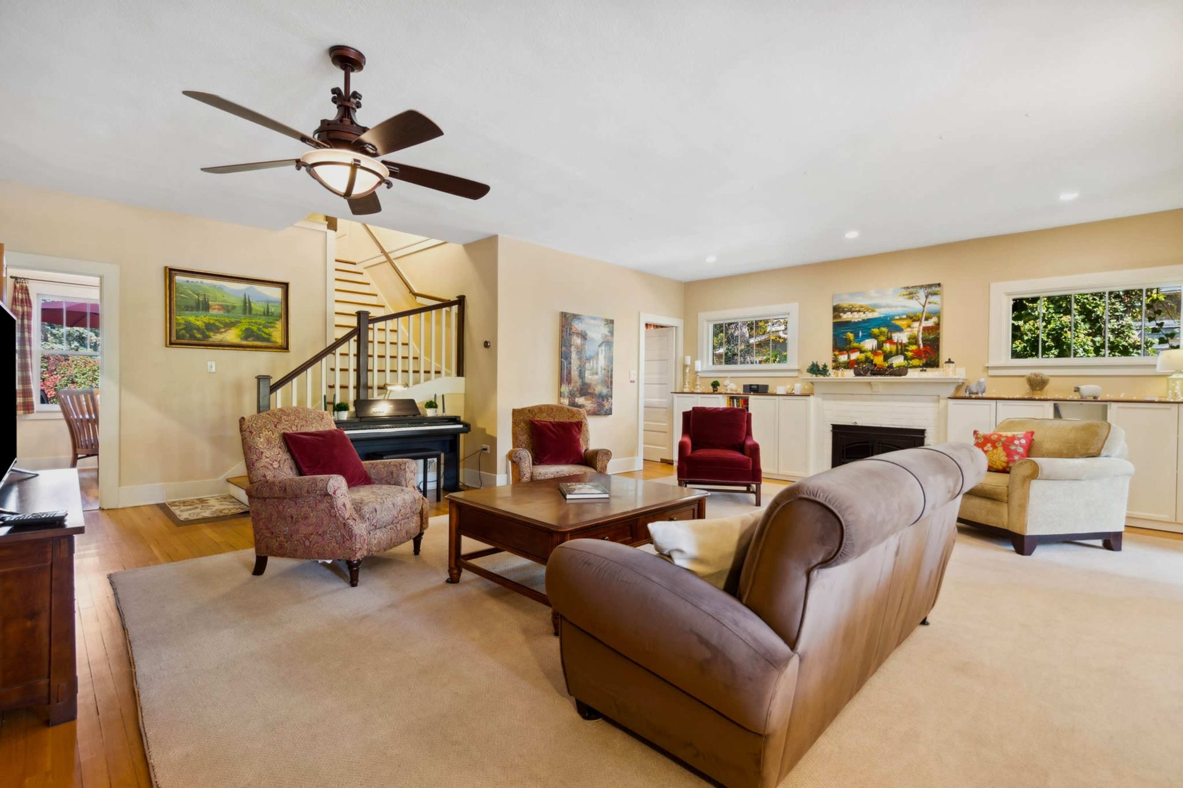 The living room features a cozy seating arrangement with two armchairs and a sofa, a coffee table in the center, and a staircase in the background leading to the upper floor.