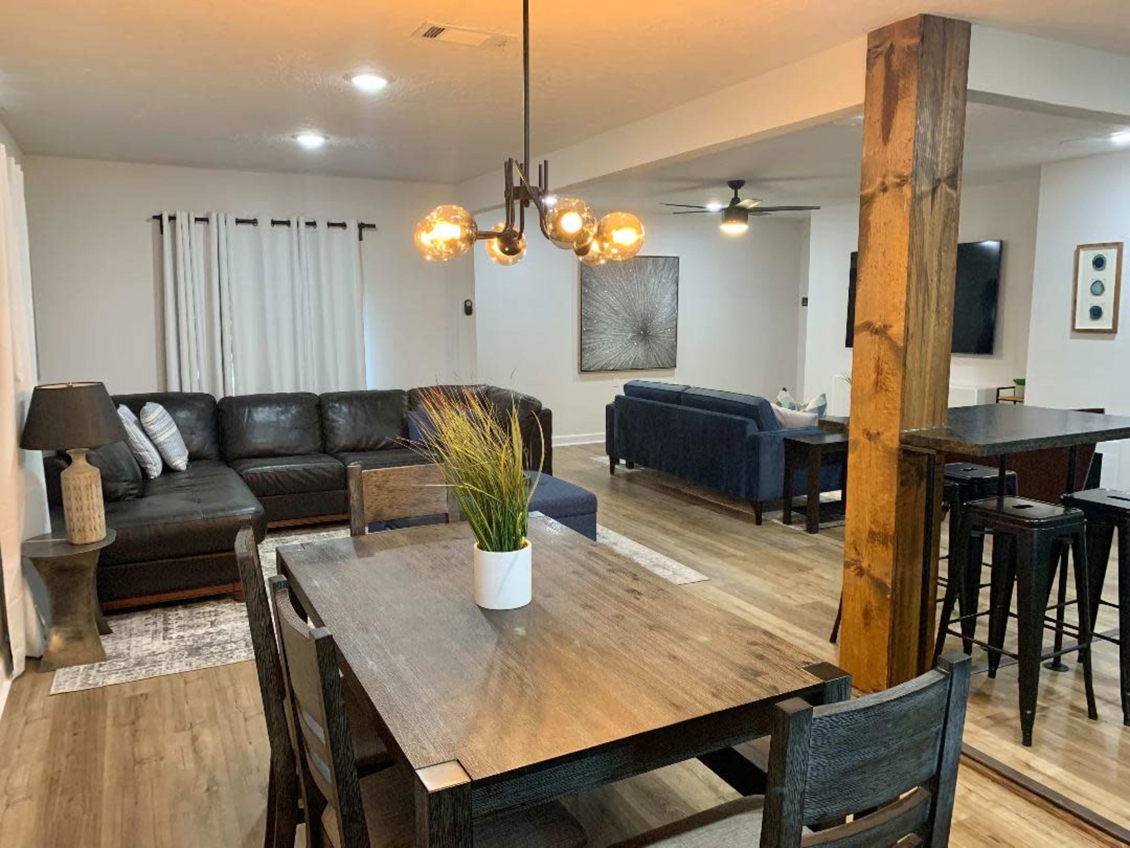 A spacious living and dining area featuring a black sectional sofa, a wooden dining table, and a ceiling fan.