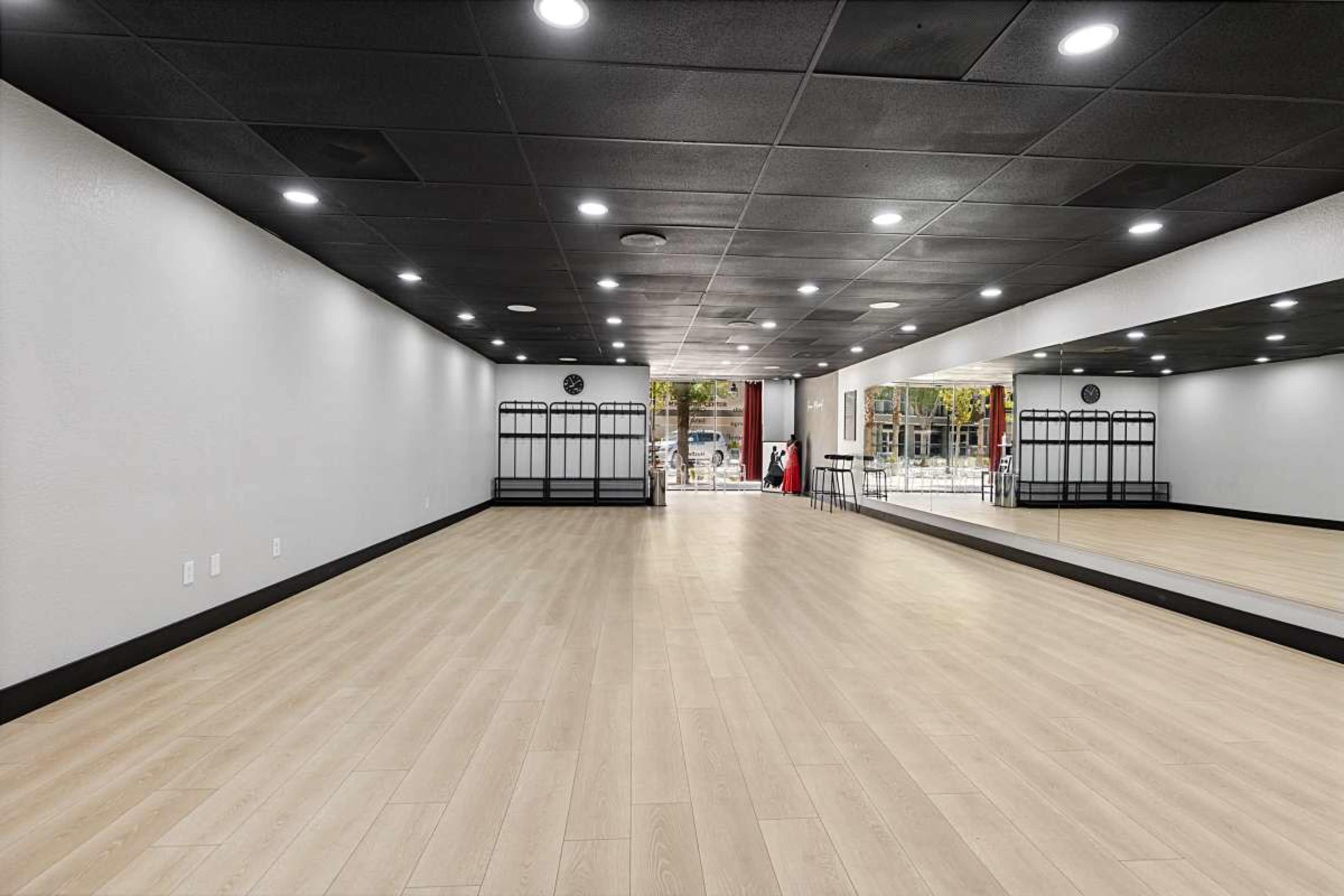 The image shows a spacious, well-lit studio with wooden flooring and large mirrors along one wall.