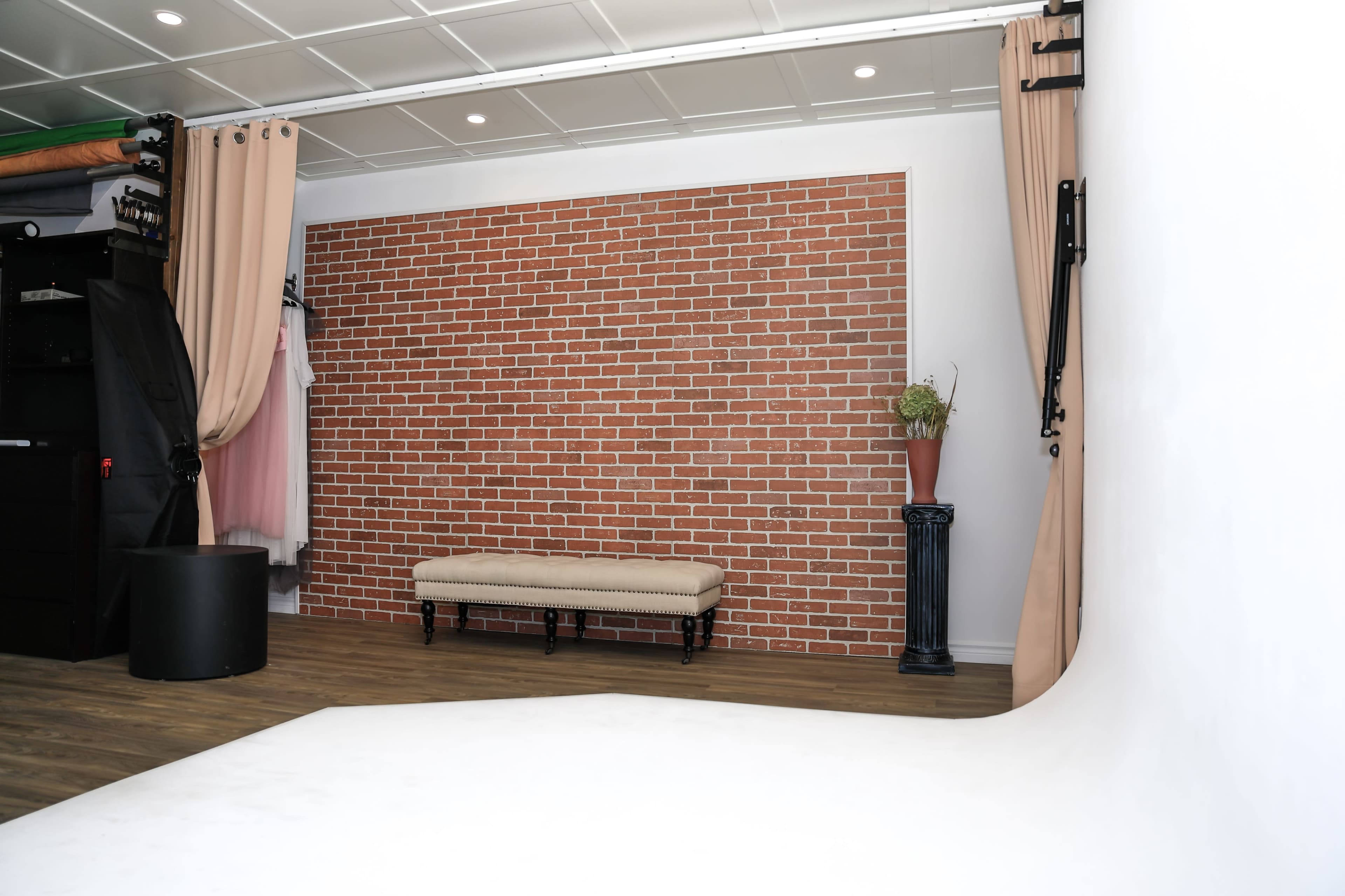 A photography studio with a brick wall backdrop, a bench in front, and a white seamless backdrop on the floor.