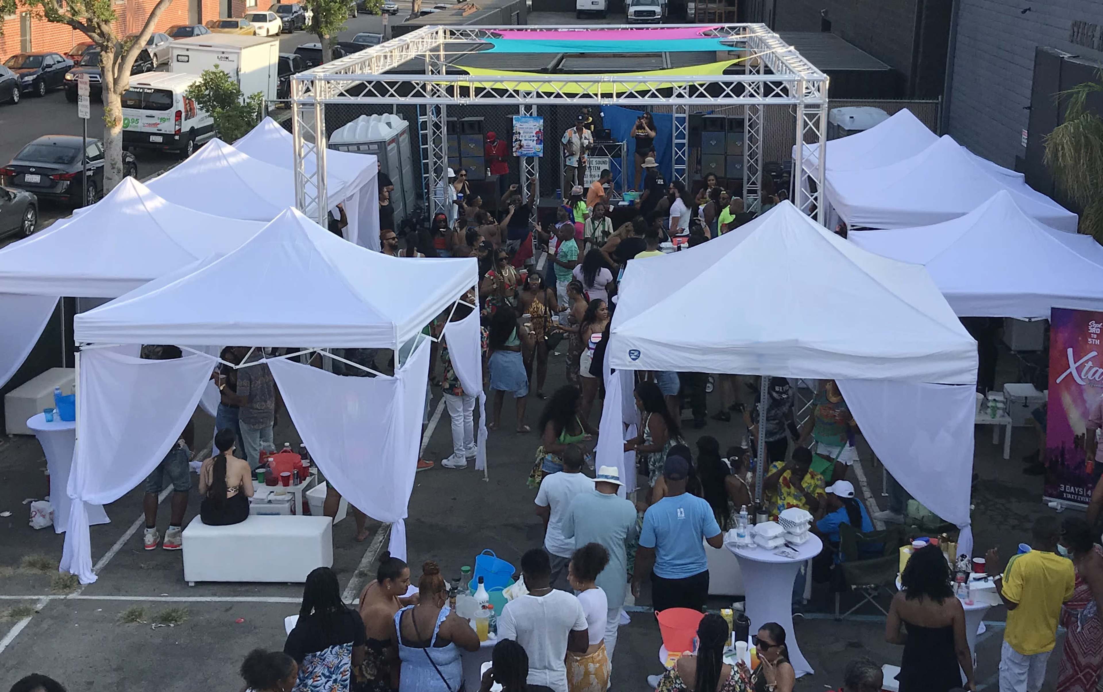 A large outdoor gathering is taking place under white tents, with a crowd of people enjoying activities and entertainment.