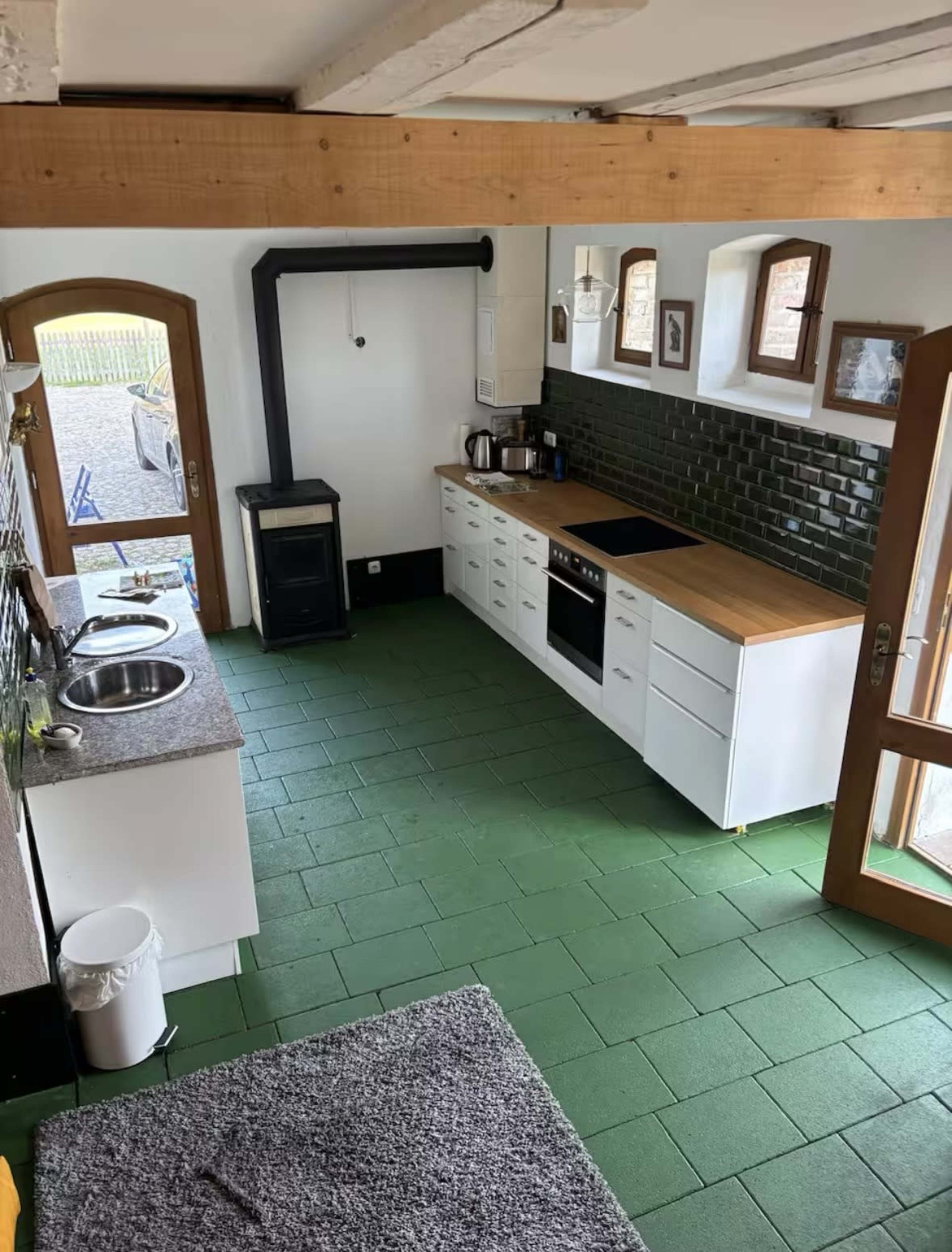 The image shows a modern kitchen with green tile flooring, a black stove, and white cabinetry, including a countertop with two sinks.
