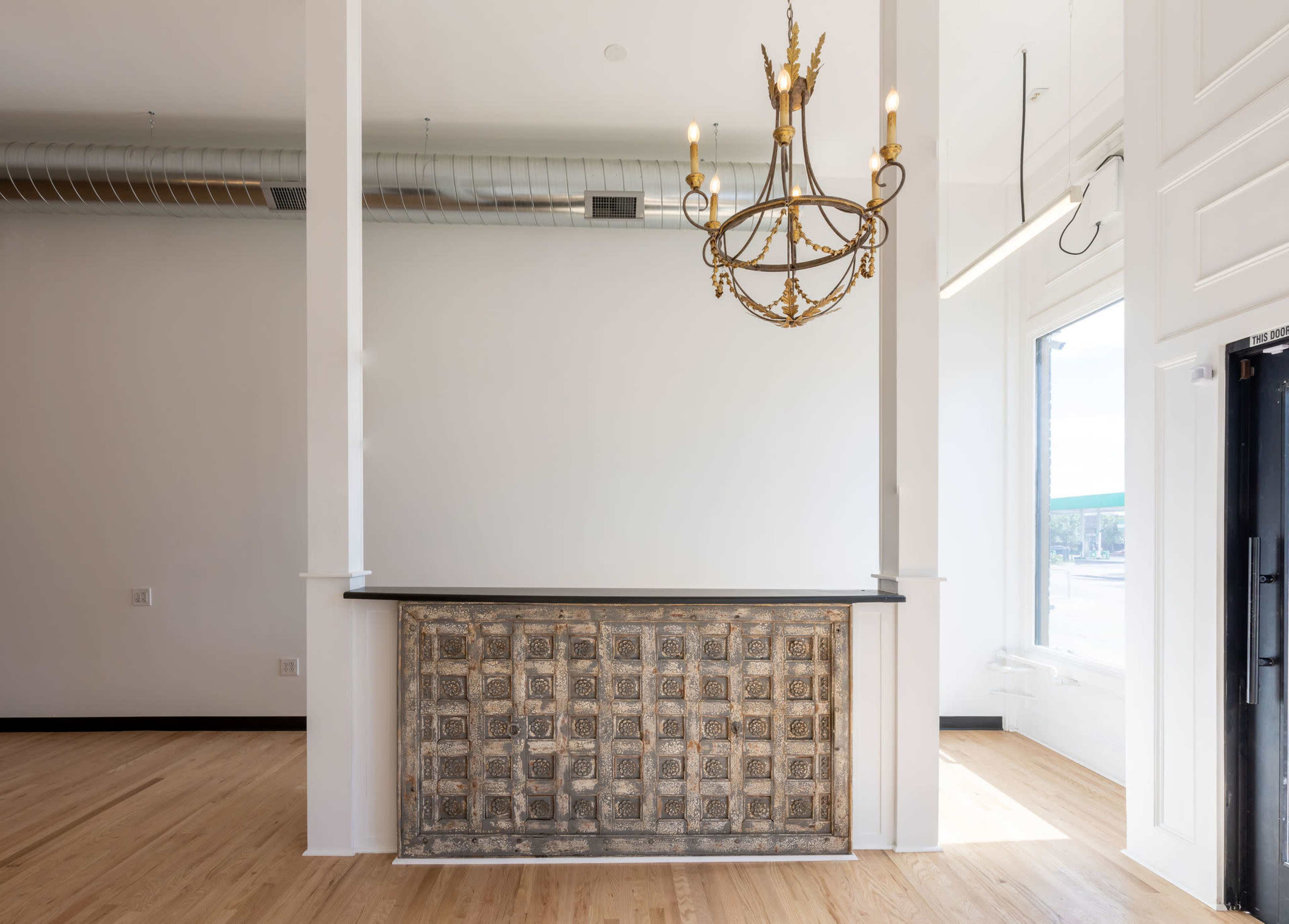A reception area with a decorative front desk and a chandelier above it, featuring large windows that provide natural light.