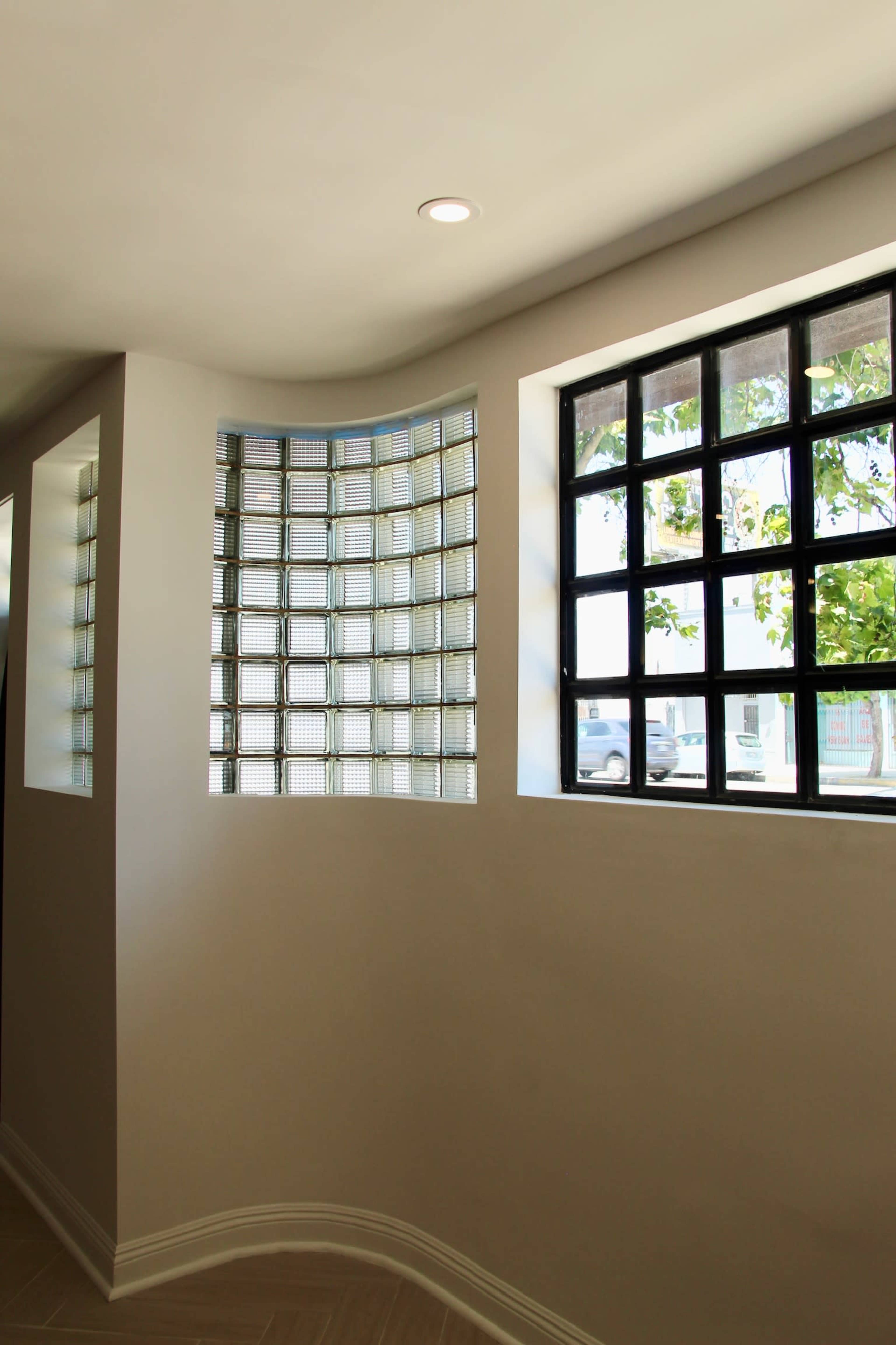 The image shows a corner of a room with one wall featuring glass block windows and another wall with a grid-style window, allowing natural light to enter.