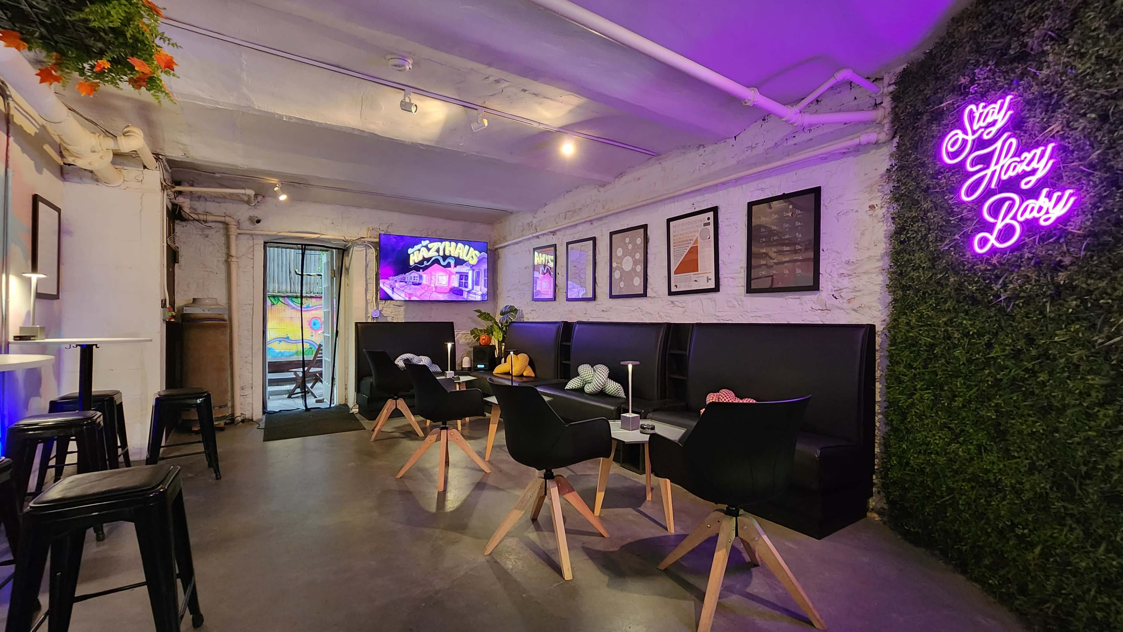 A modern cafe interior with black seating, a television displaying colorful graphics, and neon signage on a green wall.