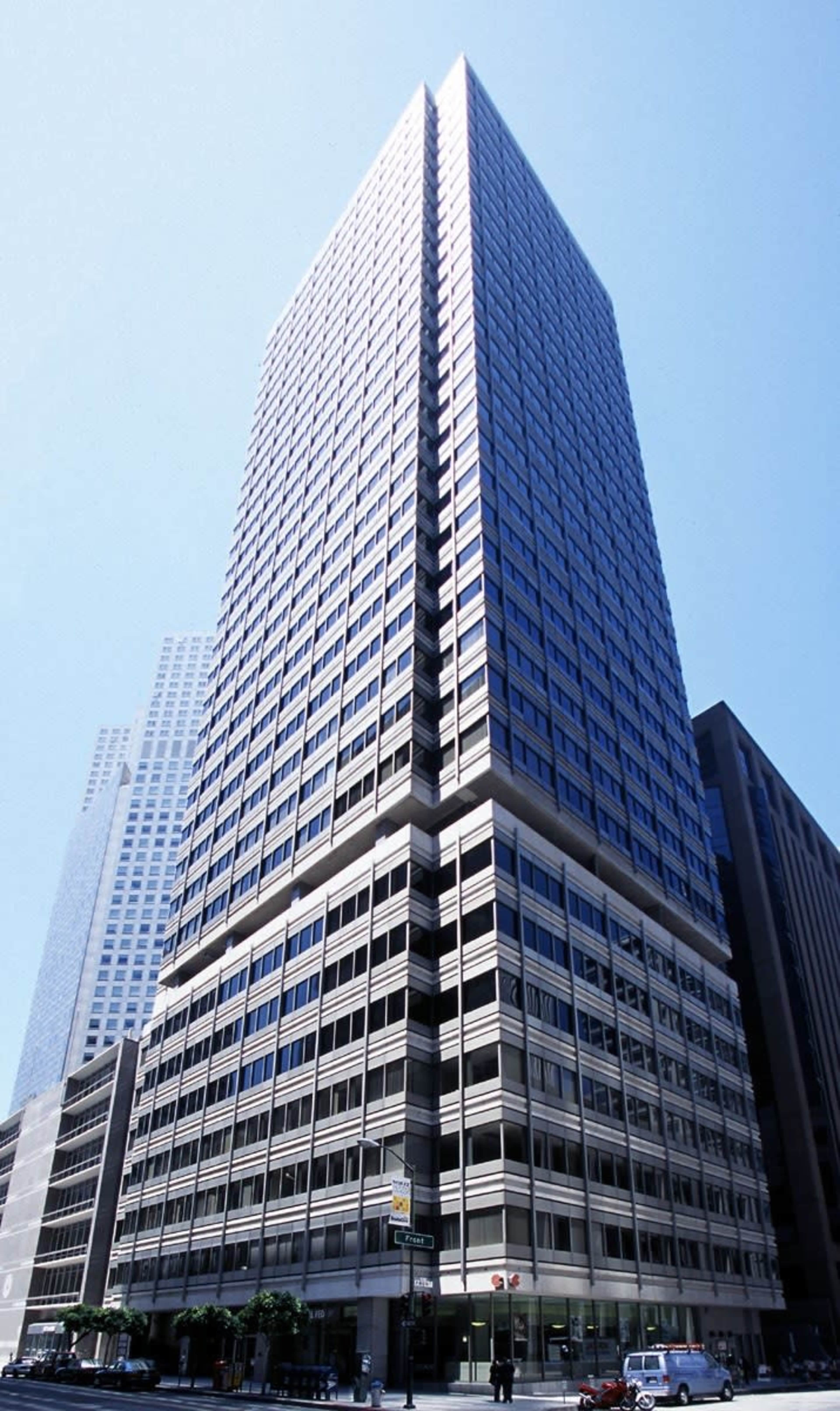 A tall, modern skyscraper with a glass and steel facade stands against a clear blue sky.