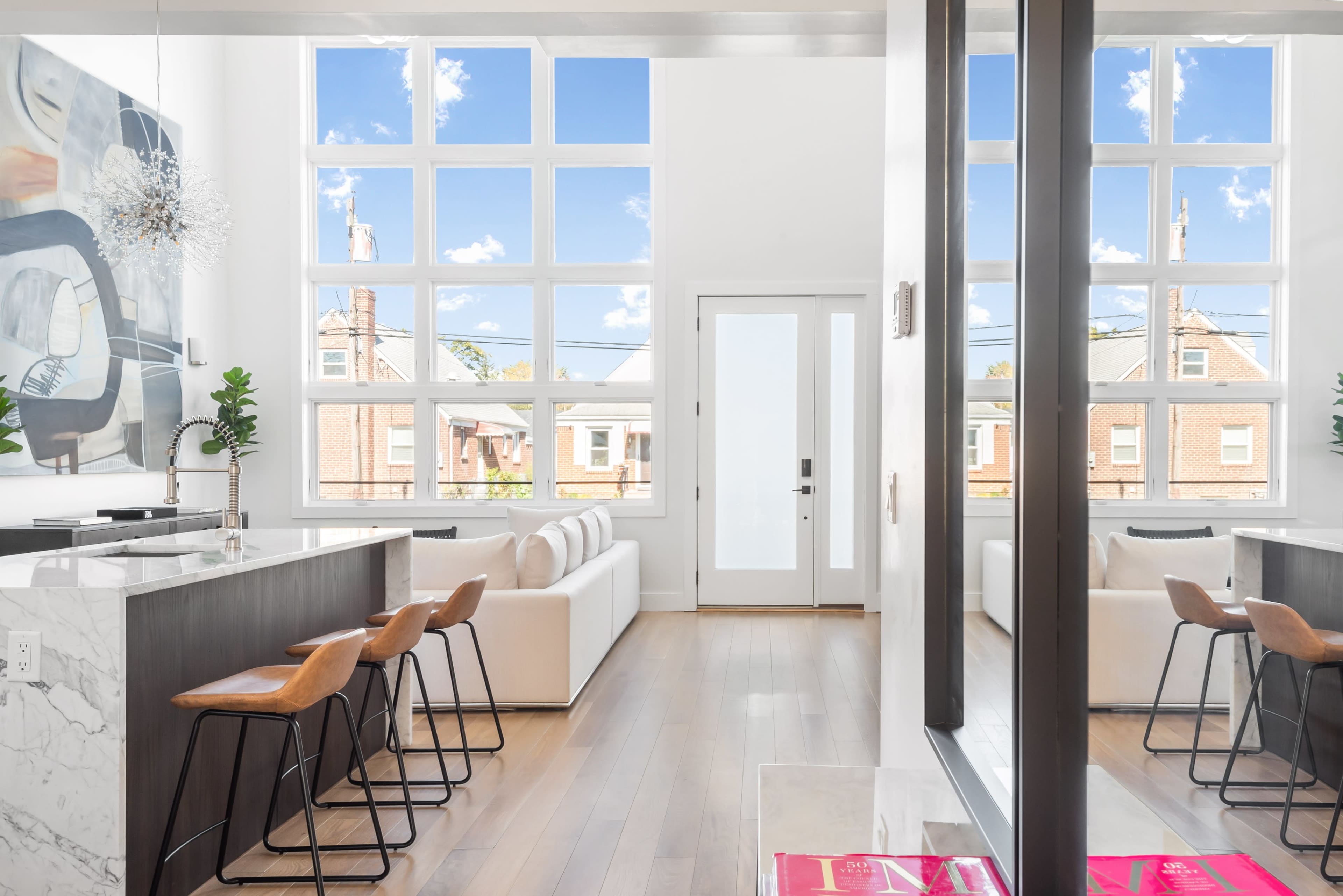 A modern living space with large windows, a kitchen island with bar stools, and a view of a bright exterior through the glass doors.