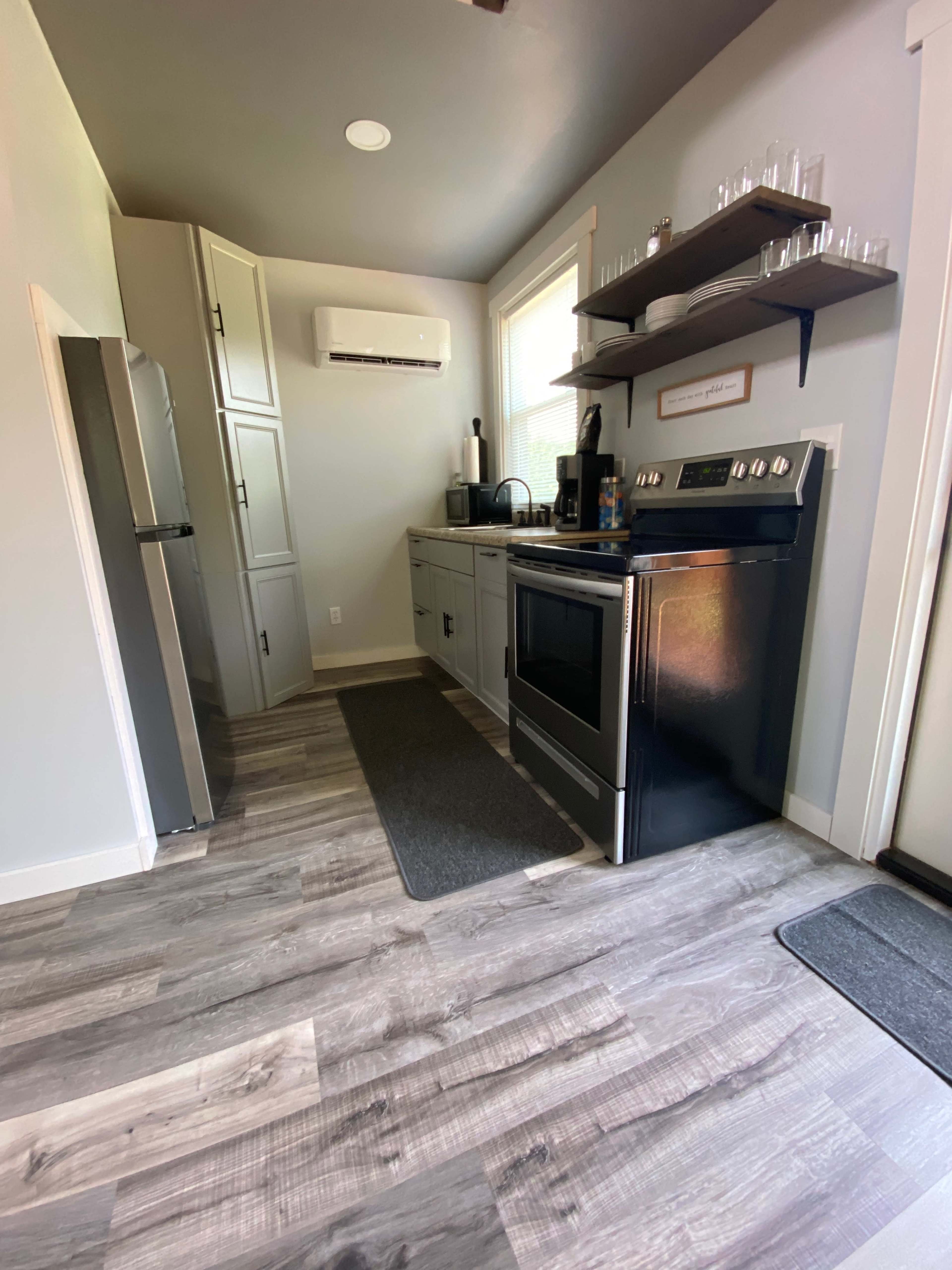 The image shows a modern kitchen with gray walls, sleek cabinetry, a stainless steel refrigerator, and a black oven, complemented by laminate flooring.
