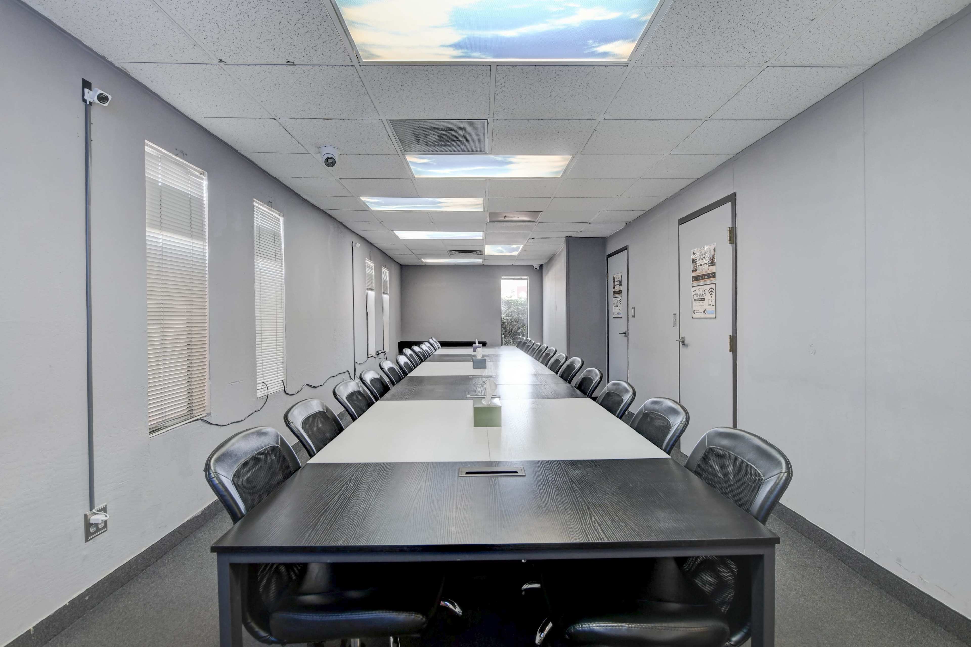 A long meeting room features a central table surrounded by black chairs, with large windows on one side and a ceiling designed to mimic a cloudy sky.