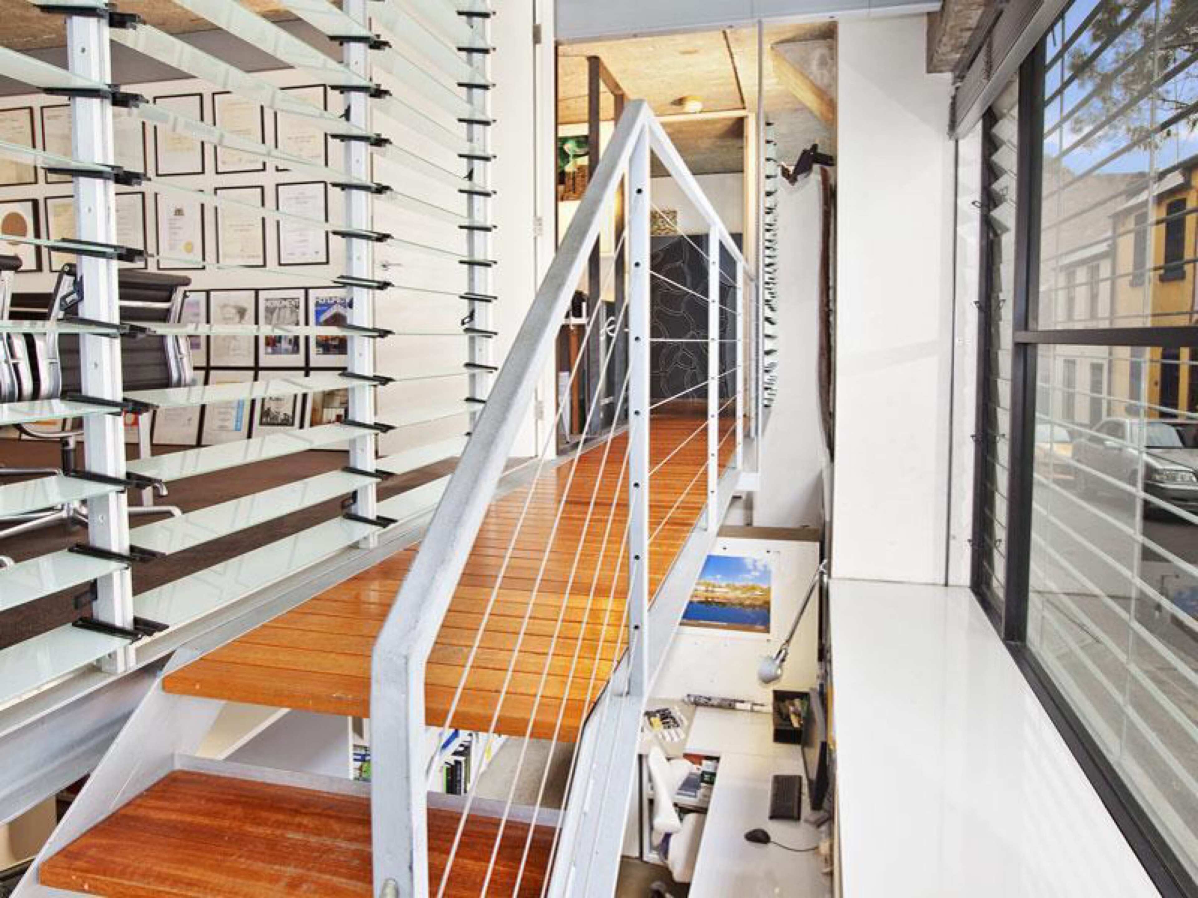 A metal staircase with wooden steps leads to an upper level, surrounded by a wall of framed artwork and large windows.