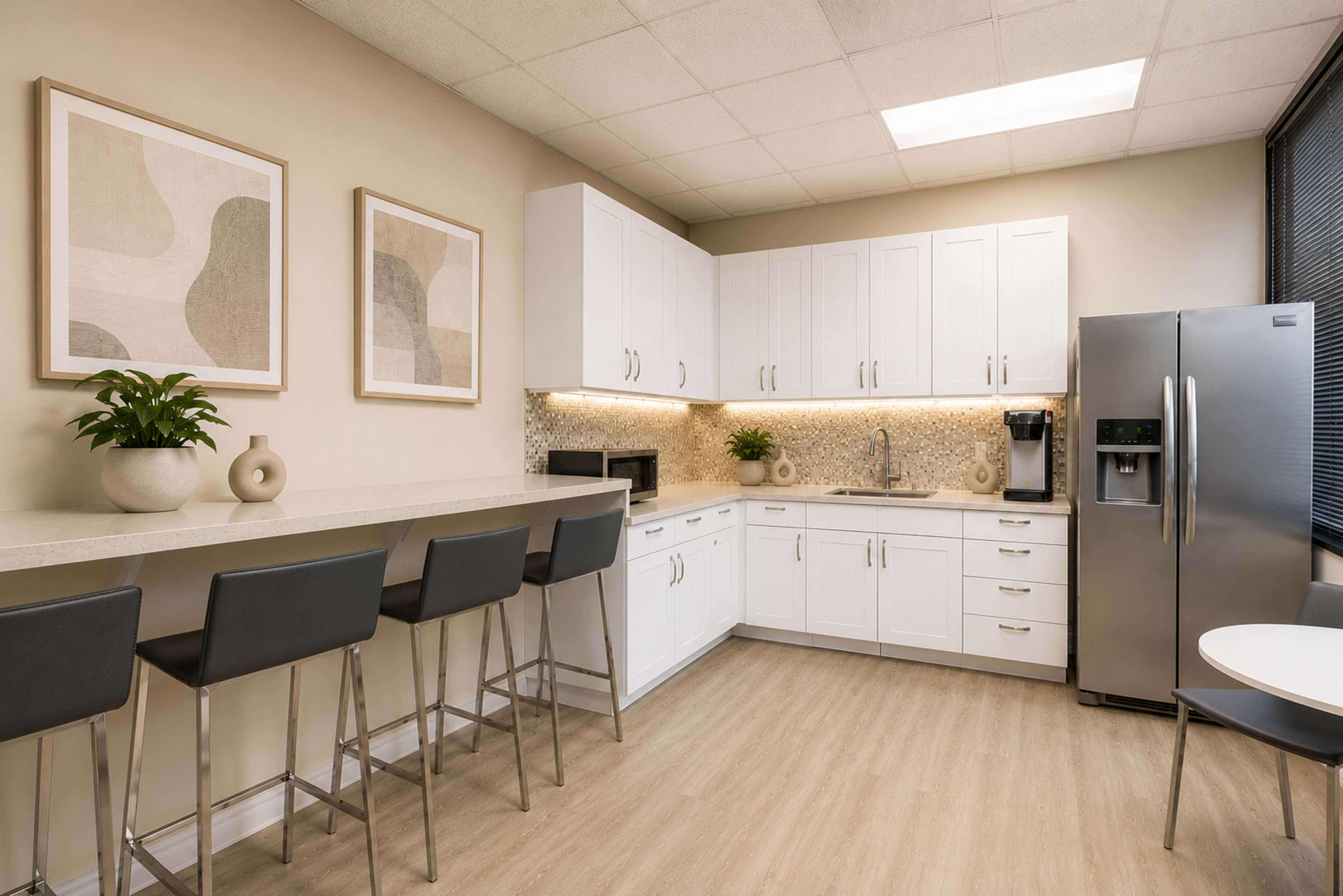 The image shows a modern kitchen with white cabinetry, a sleek refrigerator, and a seating area featuring bar stools.