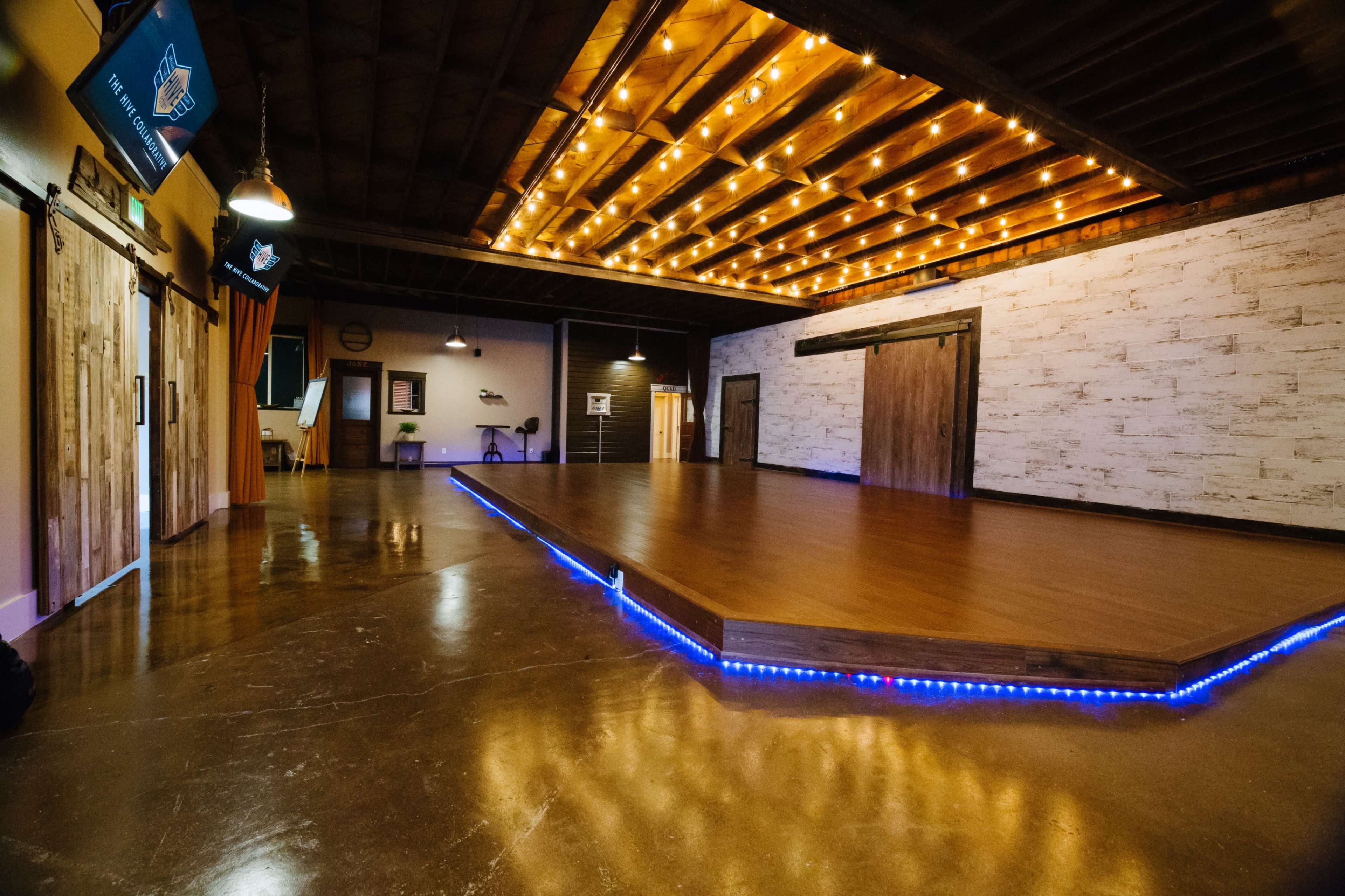 A spacious, well-lit event room featuring a polished wooden dance floor with LED lighting along the edge.