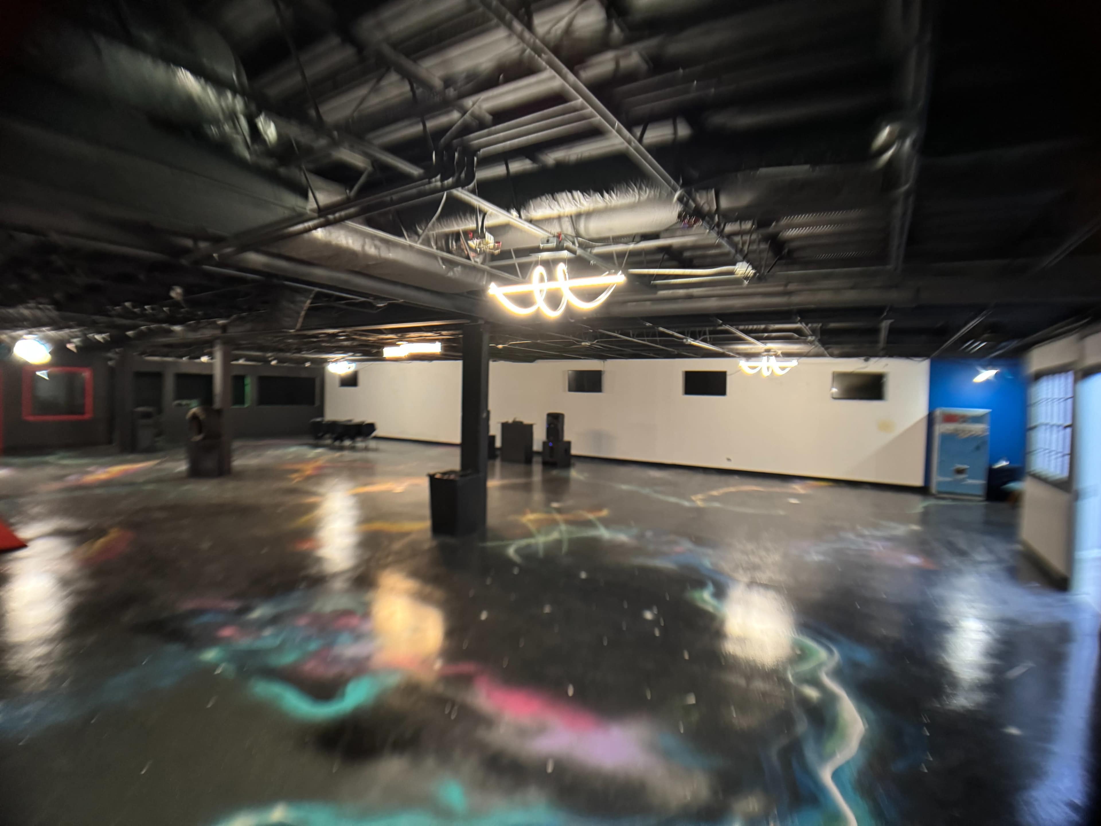 The image shows a spacious, dimly lit basement with a polished floor featuring colorful patterns and several overhead lights.