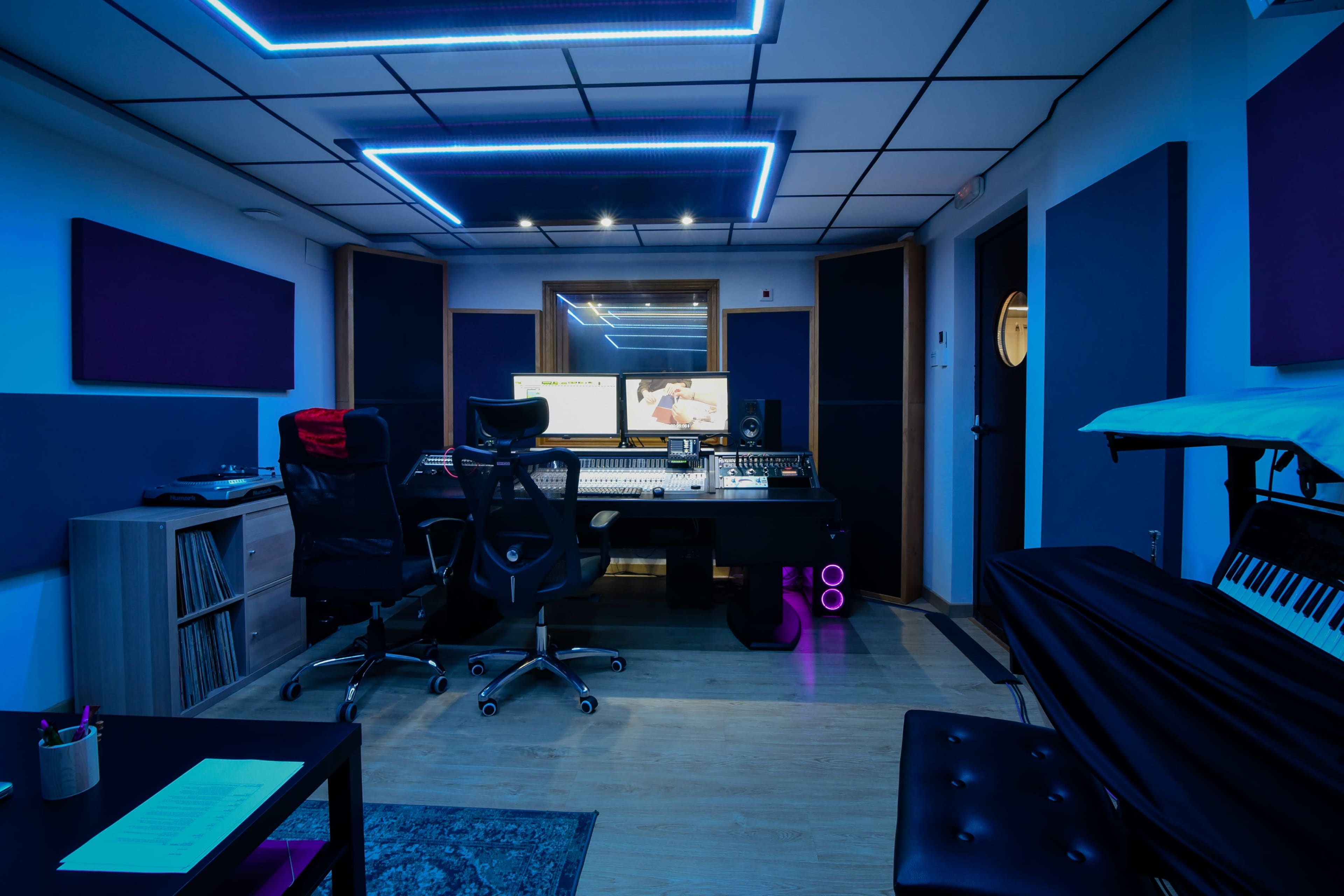 The image depicts a modern recording studio with sound equipment, a large mixing console, and ambient blue lighting.