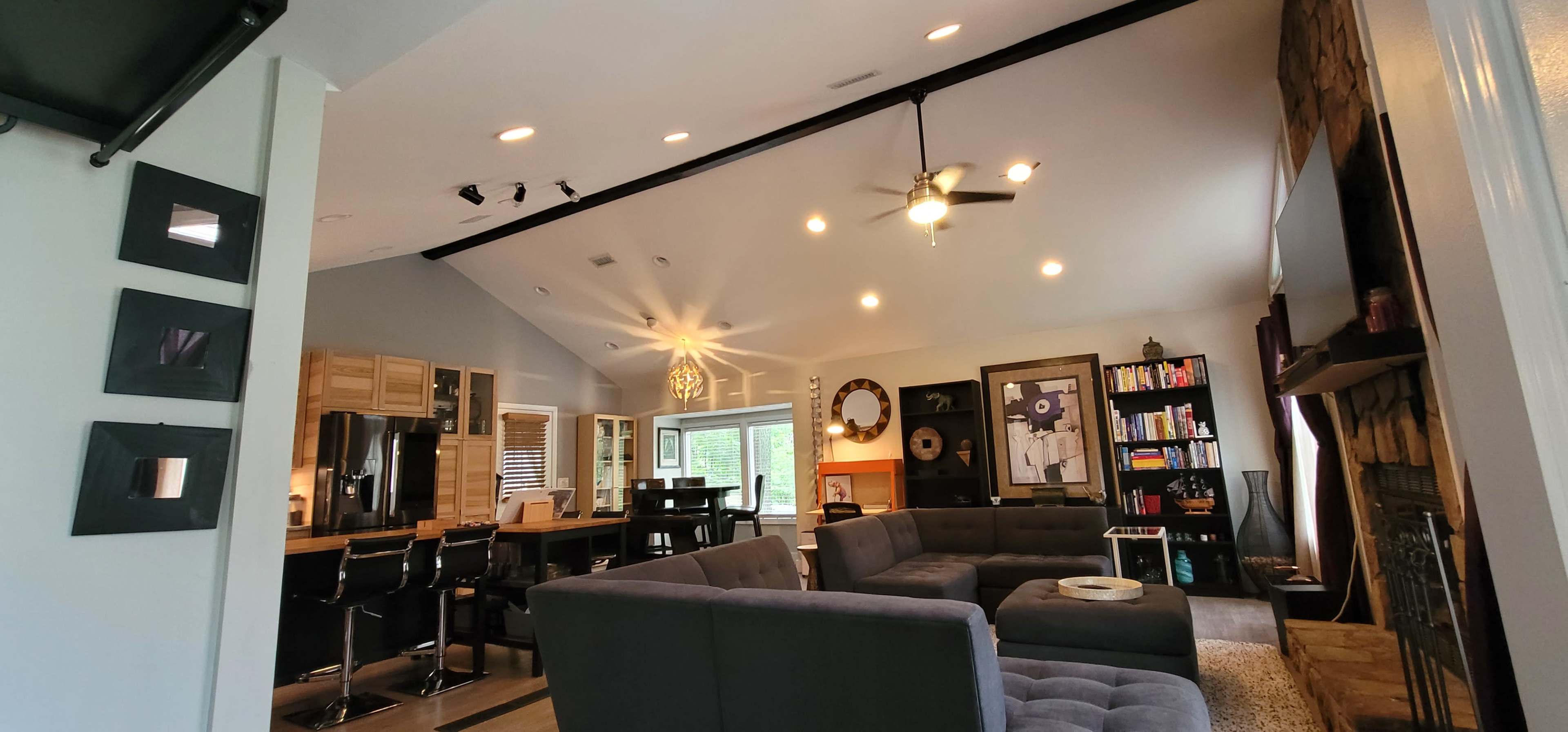 A modern living room with a gray sectional sofa, a ceiling fan, and a combination of wood and stone elements, featuring a large window that lets in natural light.