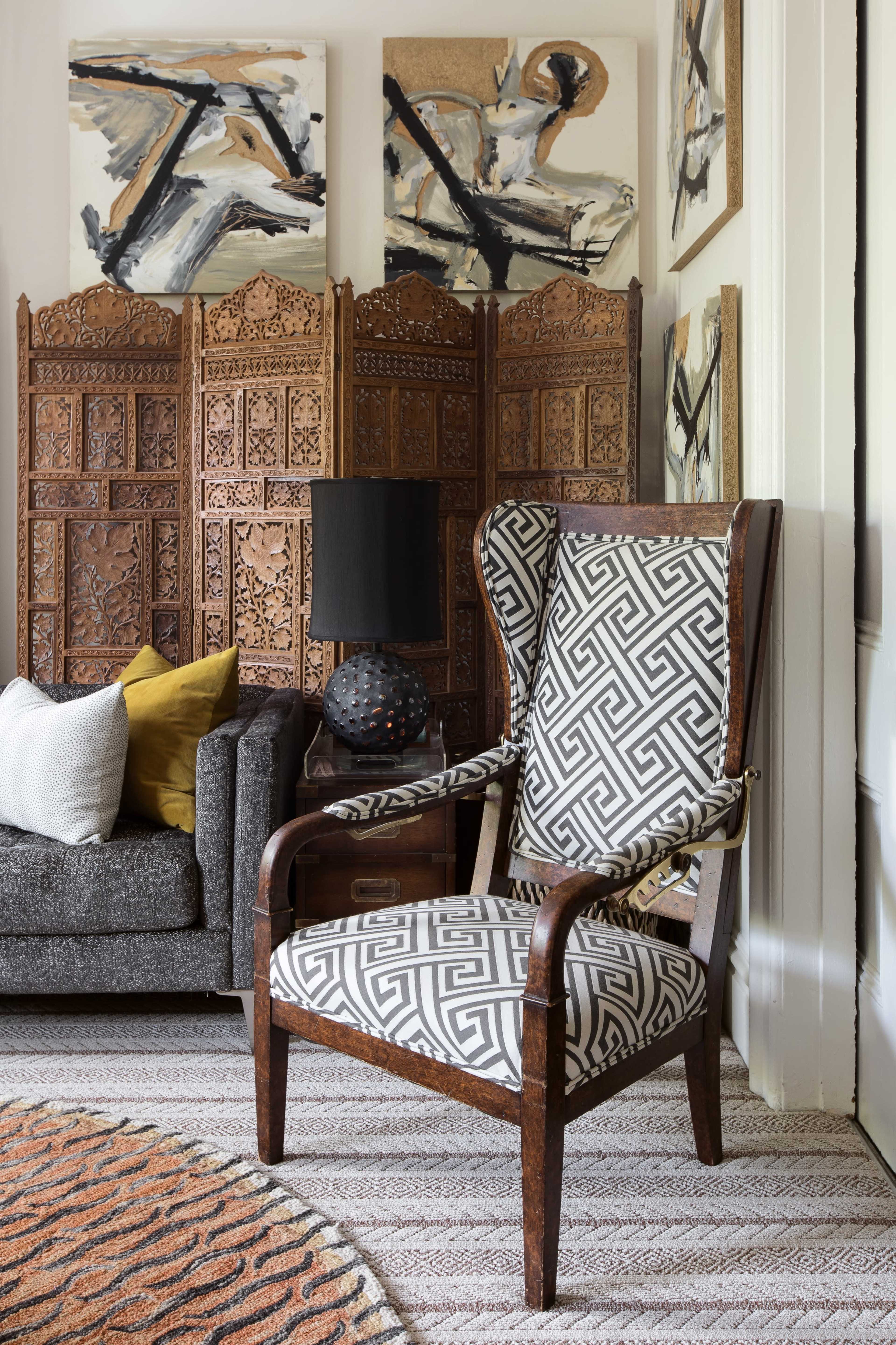 The scene features a patterned armchair beside a textured gray sofa, with wooden decorative panels and abstract artwork in the background.