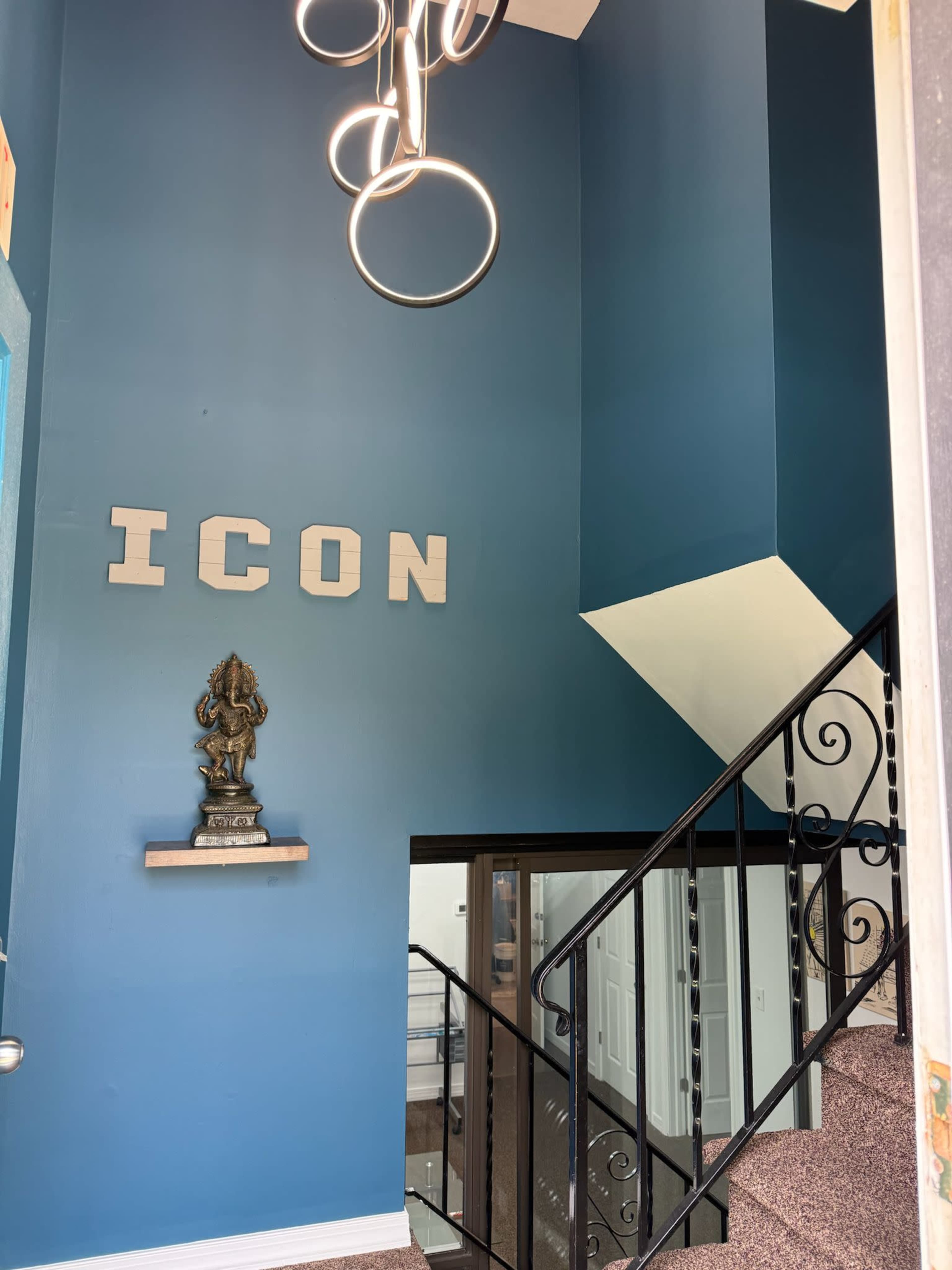 The image shows a brightly colored wall with the word "ICON" displayed, a decorative statue on a shelf, and a staircase leading to another level, accompanied by a modern light fixture.