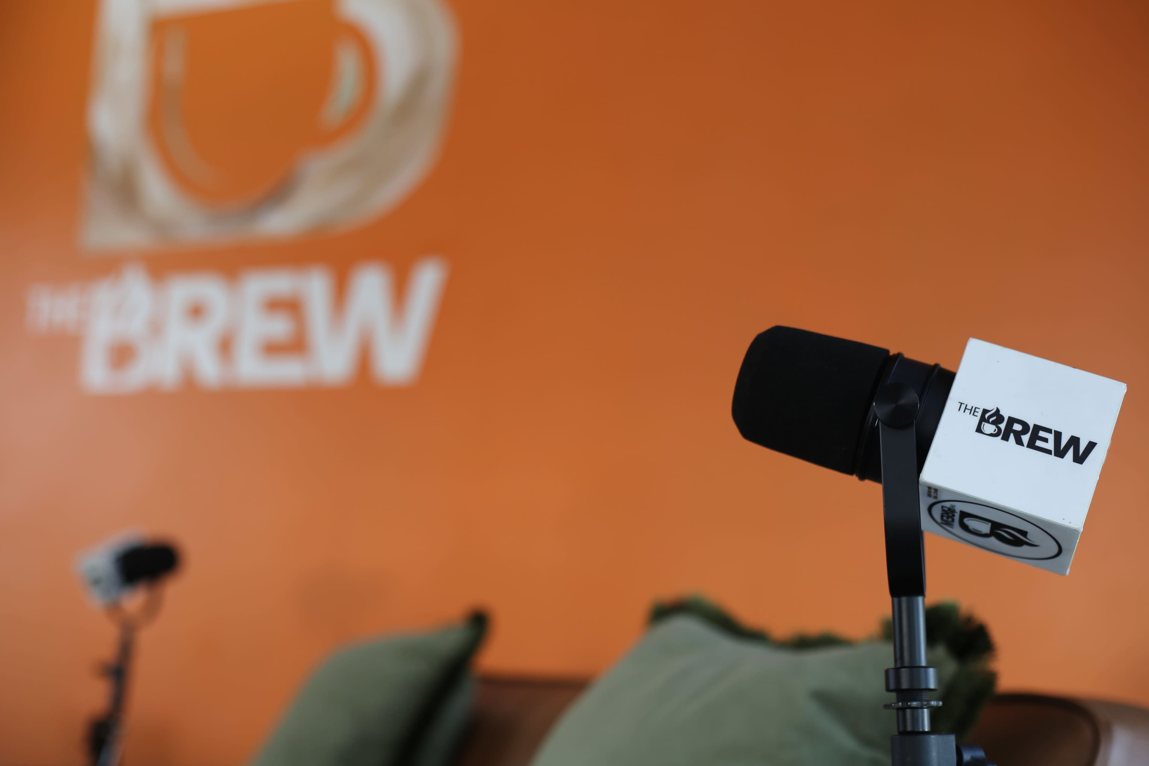 A microphone on a stand is positioned in front of an orange wall featuring the text "THE BREW."