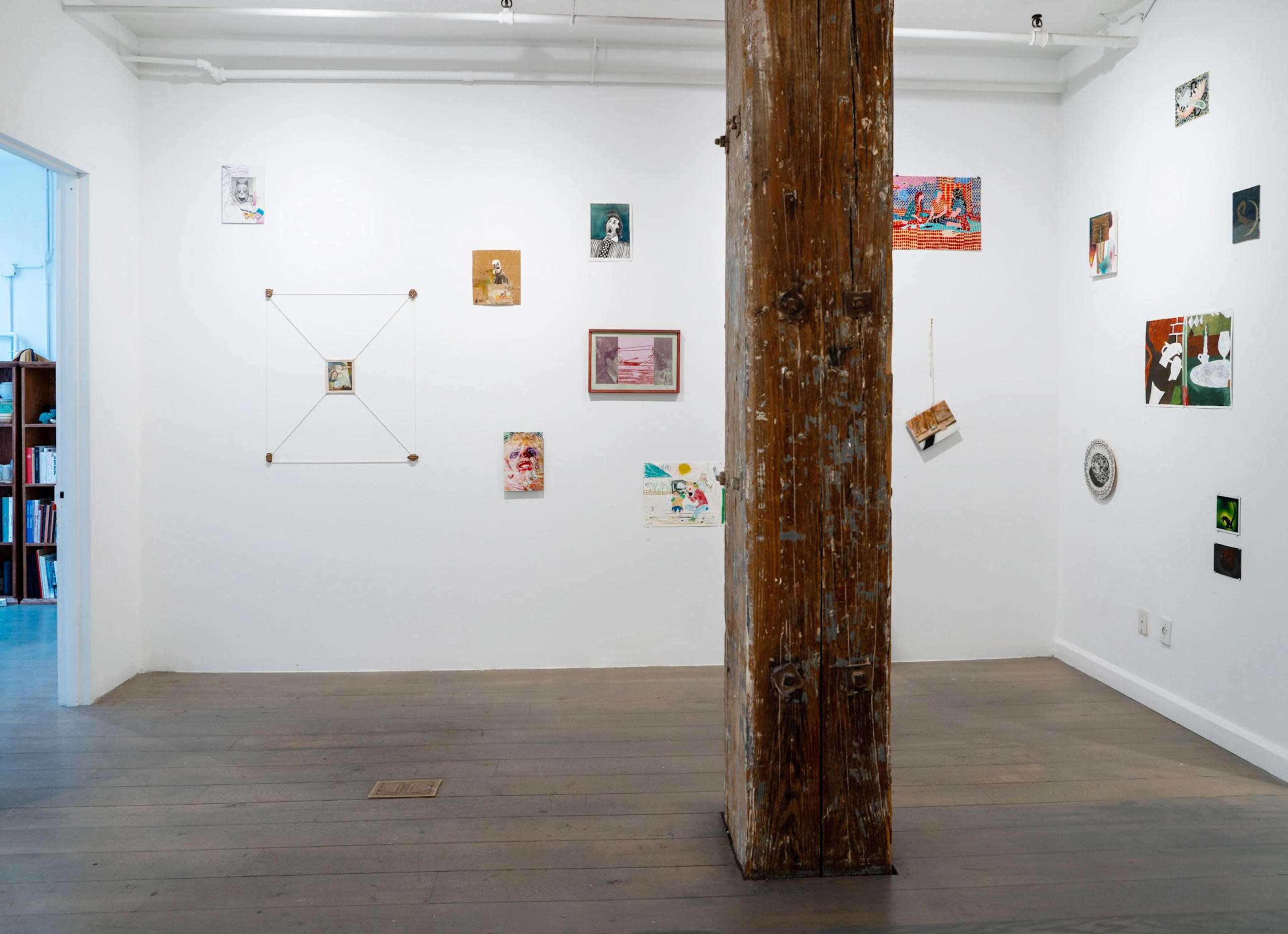 The image depicts an art gallery with white walls showcasing various artworks, with a prominent wooden column in the center.